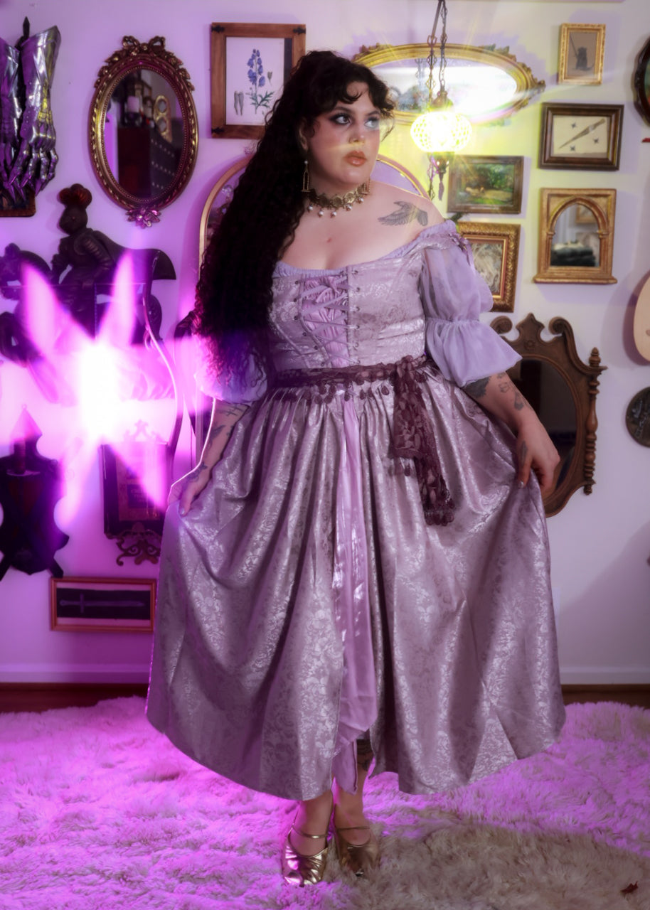Woman wearing a lavender floral satin corset dress with puff sleeves in a vintage-style room with framed art on walls