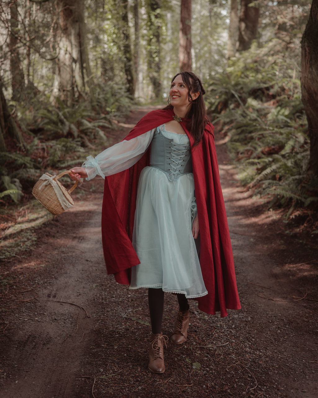 Woman wearing a red linen renaissance cloak walking through a forest path holding a wicker basket on an autumn day