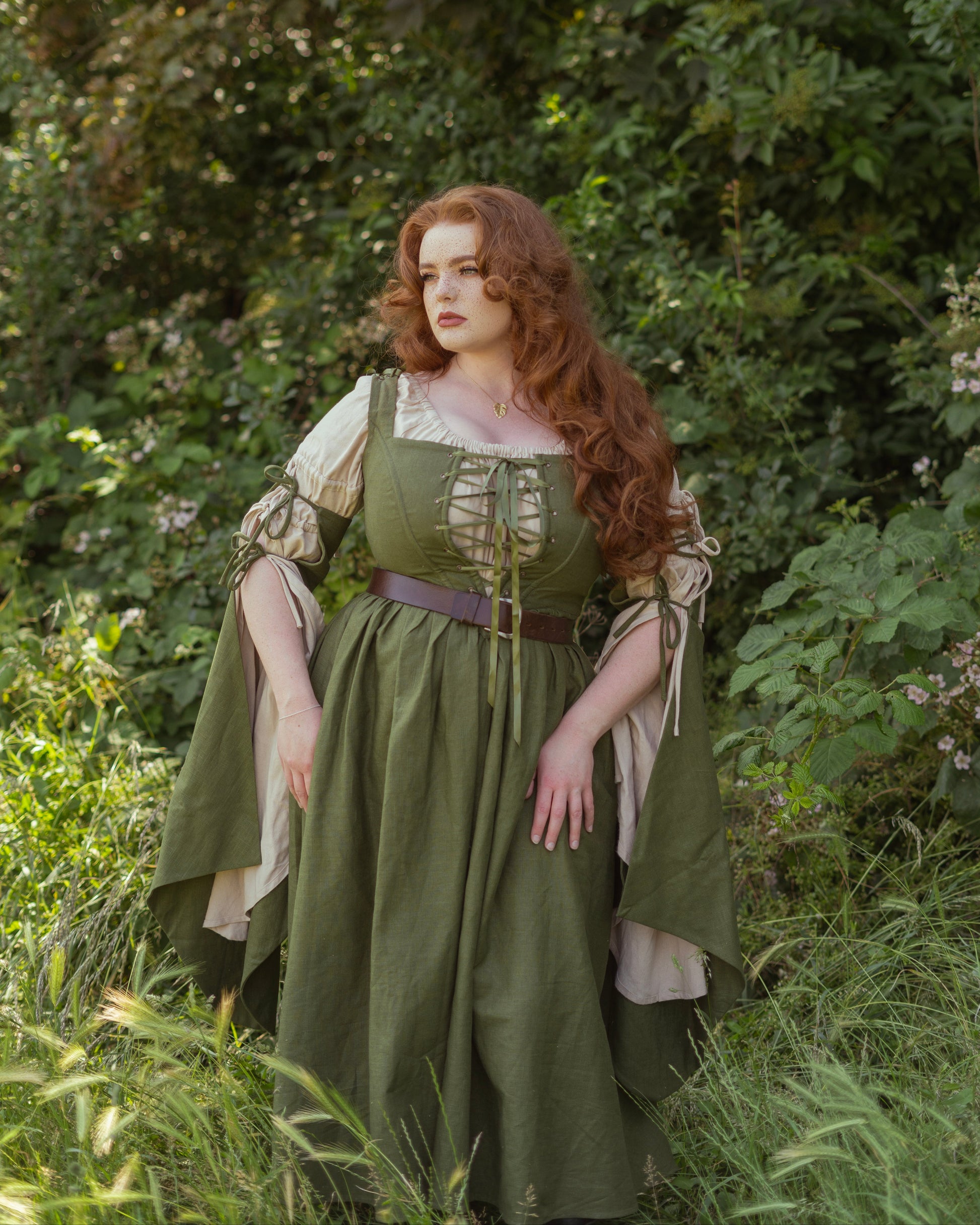 Woman in a green dress standing in a natural setting with trees and grass.
