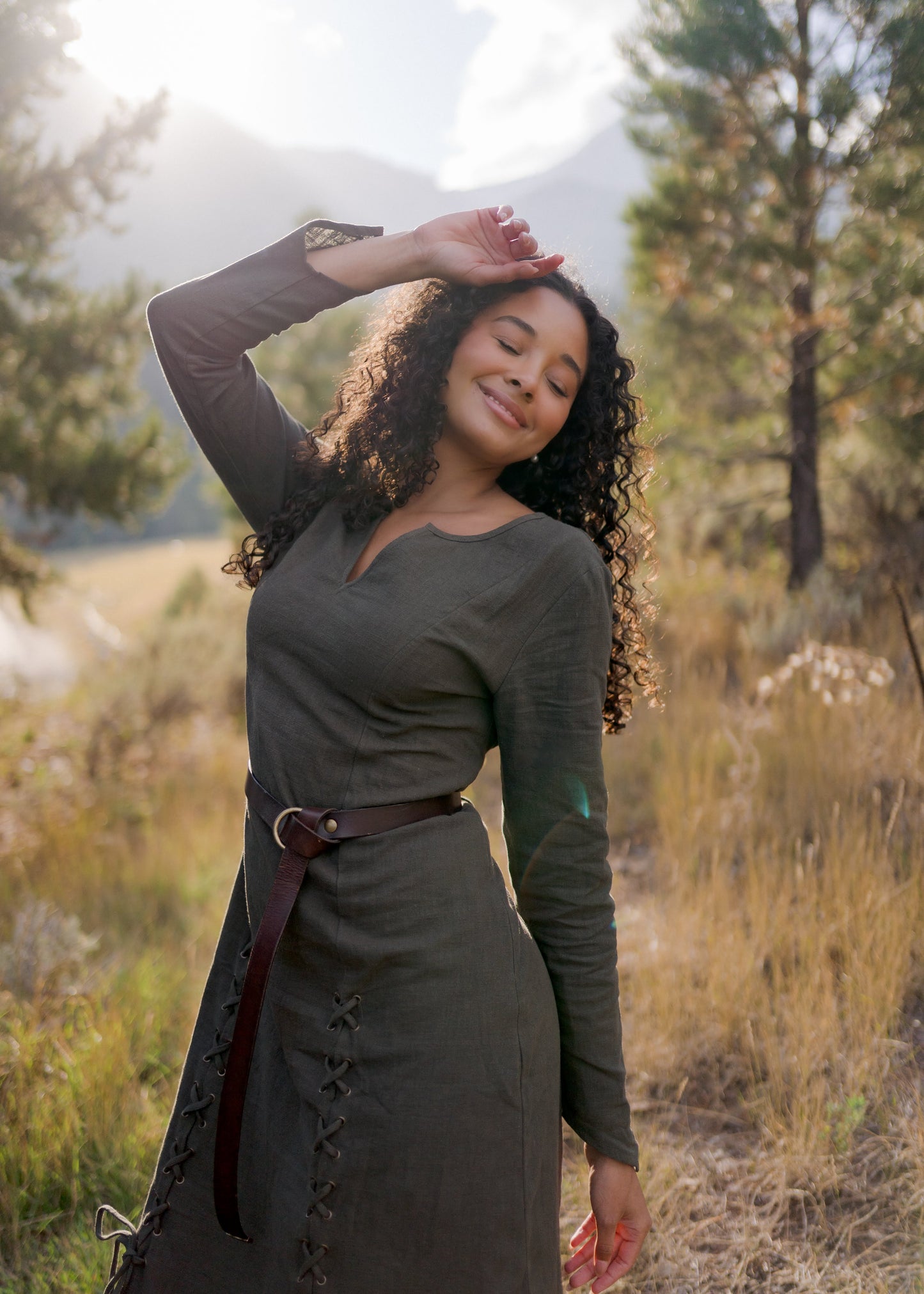 Olive Green Viking Dress with fitted silhouette, pointed sleeves and laced front detail shown outdoors in natural mountain setting