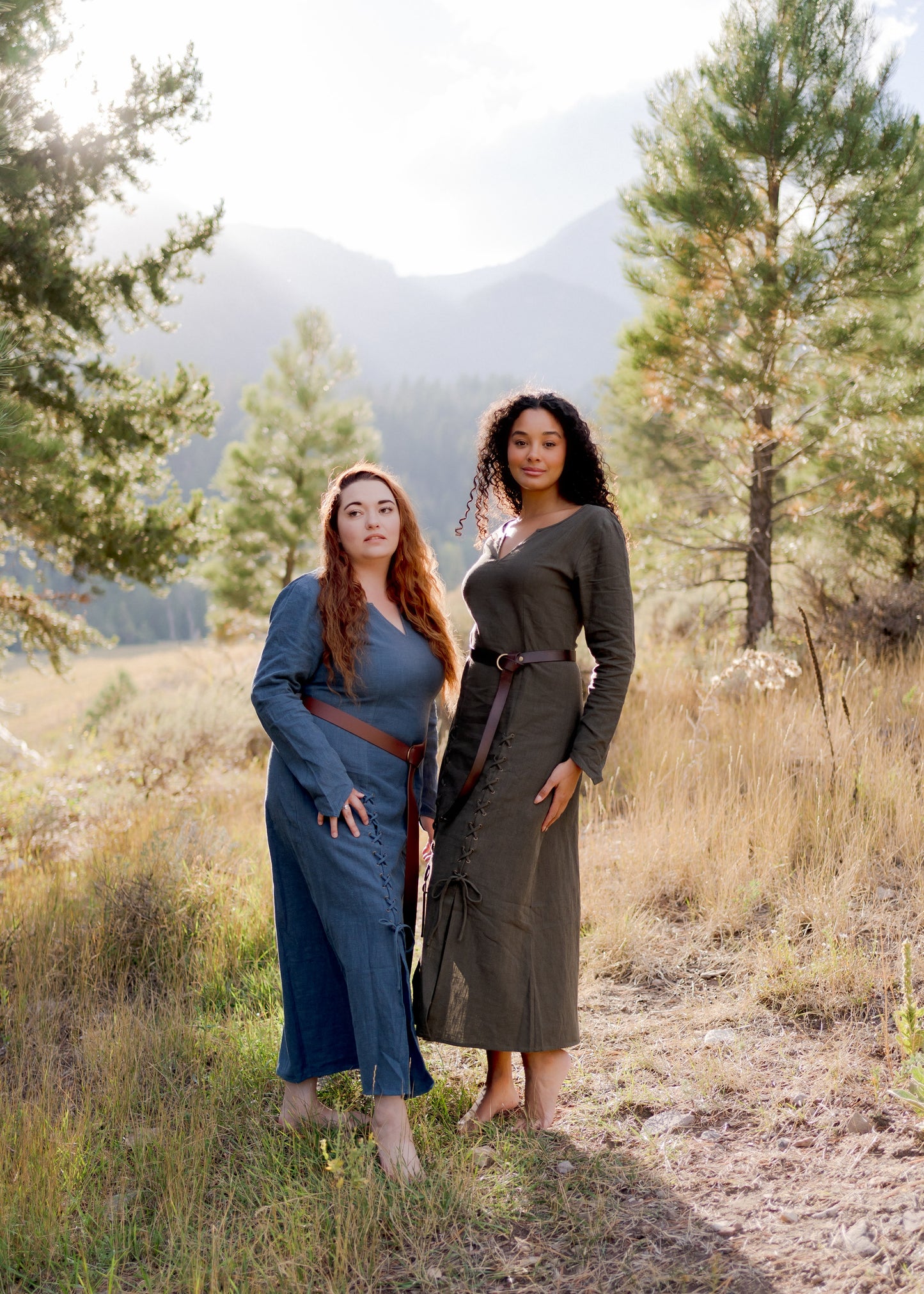 Olive Green Viking Dress shown in mountain setting with medieval-style lacing and fitted silhouette, displayed outdoors with pine trees