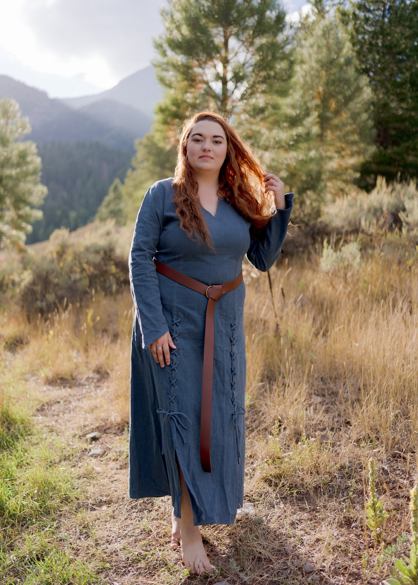 Teal Viking Dress shown outdoors in mountain setting, featuring fitted silhouette, laced front detail and leather belt against nature backdrop