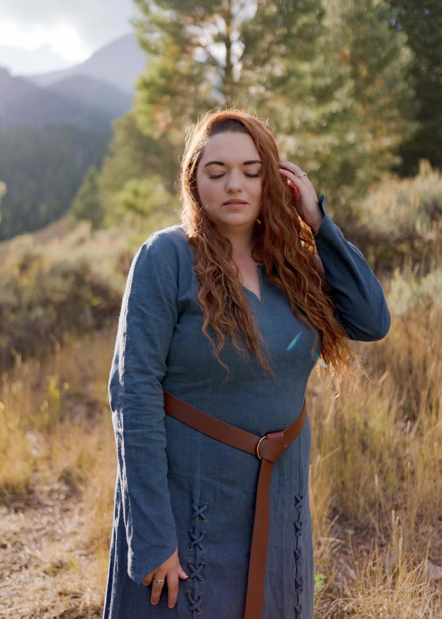 Teal Viking dress with front lacing and brown belt shown outdoors against mountain backdrop in golden sunlight