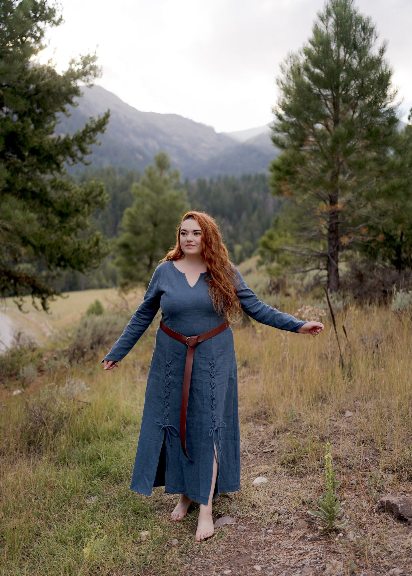 Teal Viking Dress shown in outdoor mountain setting with laced front detail and leather belt against forest backdrop