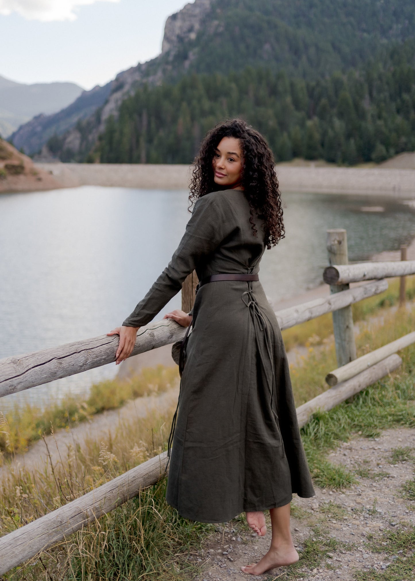 Olive Green Viking Dress shown by lake with mountains, featuring back lacing detail and long skirt in natural outdoor setting