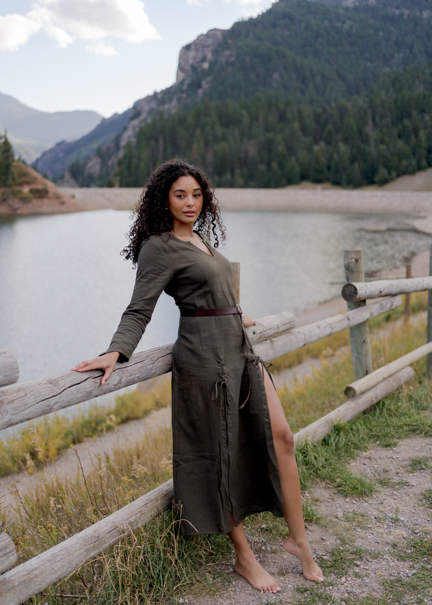 Olive Green Viking Dress shown outdoors against mountain lake backdrop, featuring laced side slit and fitted long sleeves