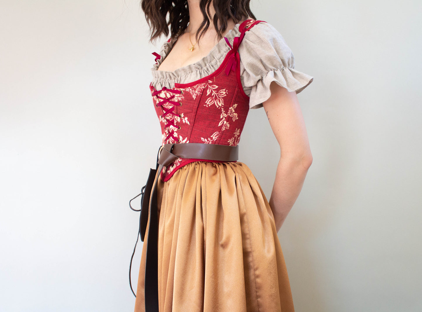 Woman wearing a Handmade Dark Red Toile Corset with floral pattern and beige puff sleeve blouse standing sideways