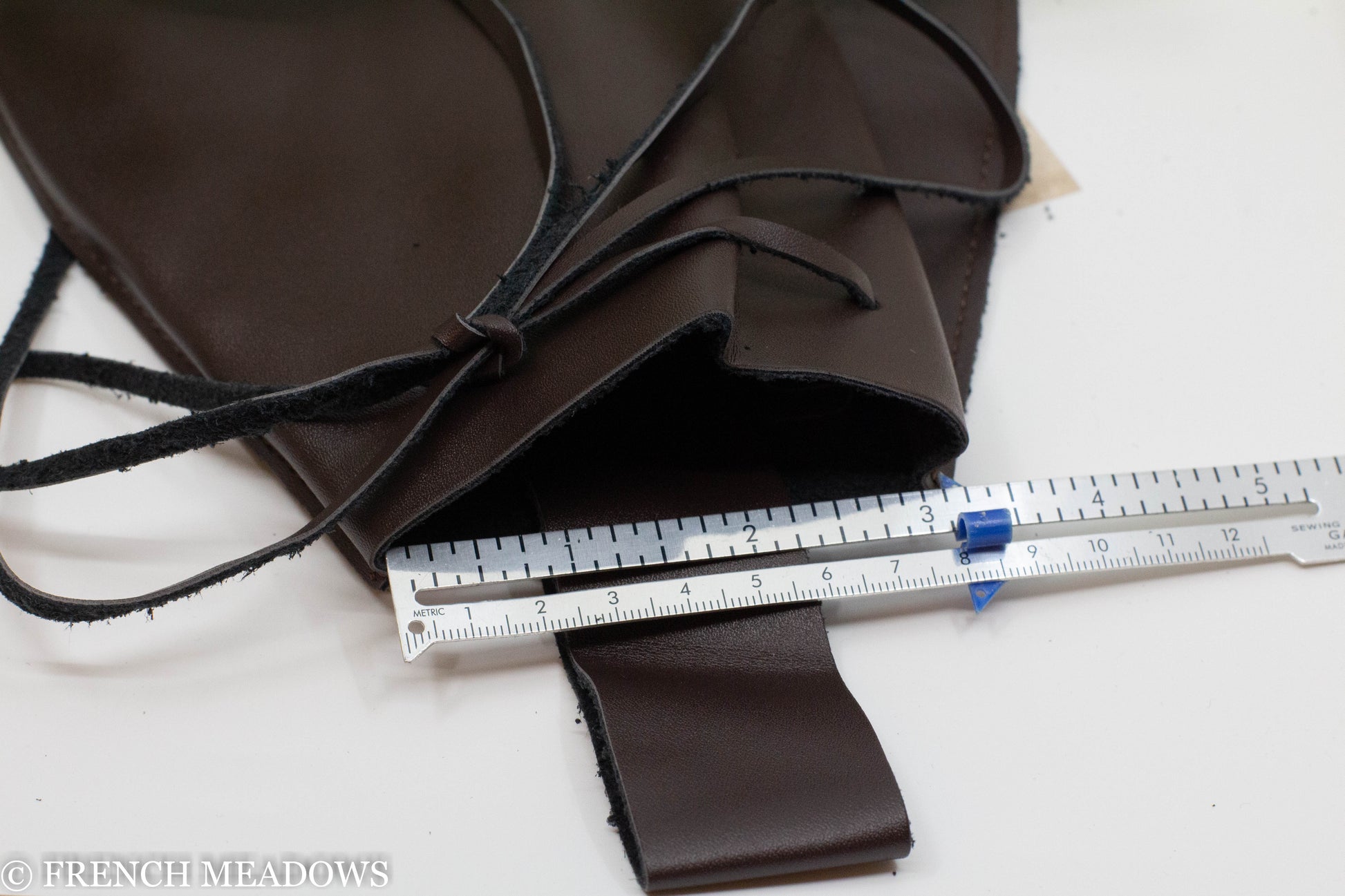 Brown vegan leather drawstring pouch shown with measuring ruler for belt attachment up to 3 inches wide.