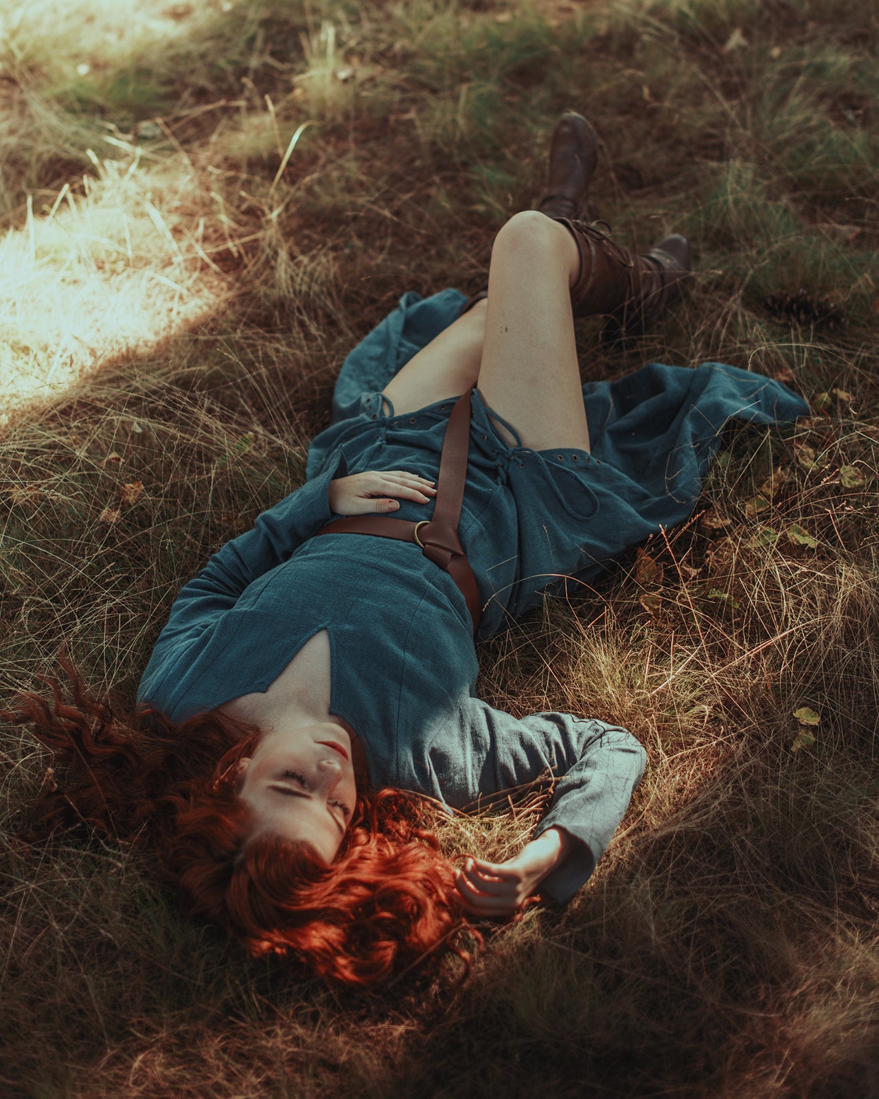 Teal Viking Dress lying on autumn grass in warm sunlight, showcasing medieval style and front lacing detail