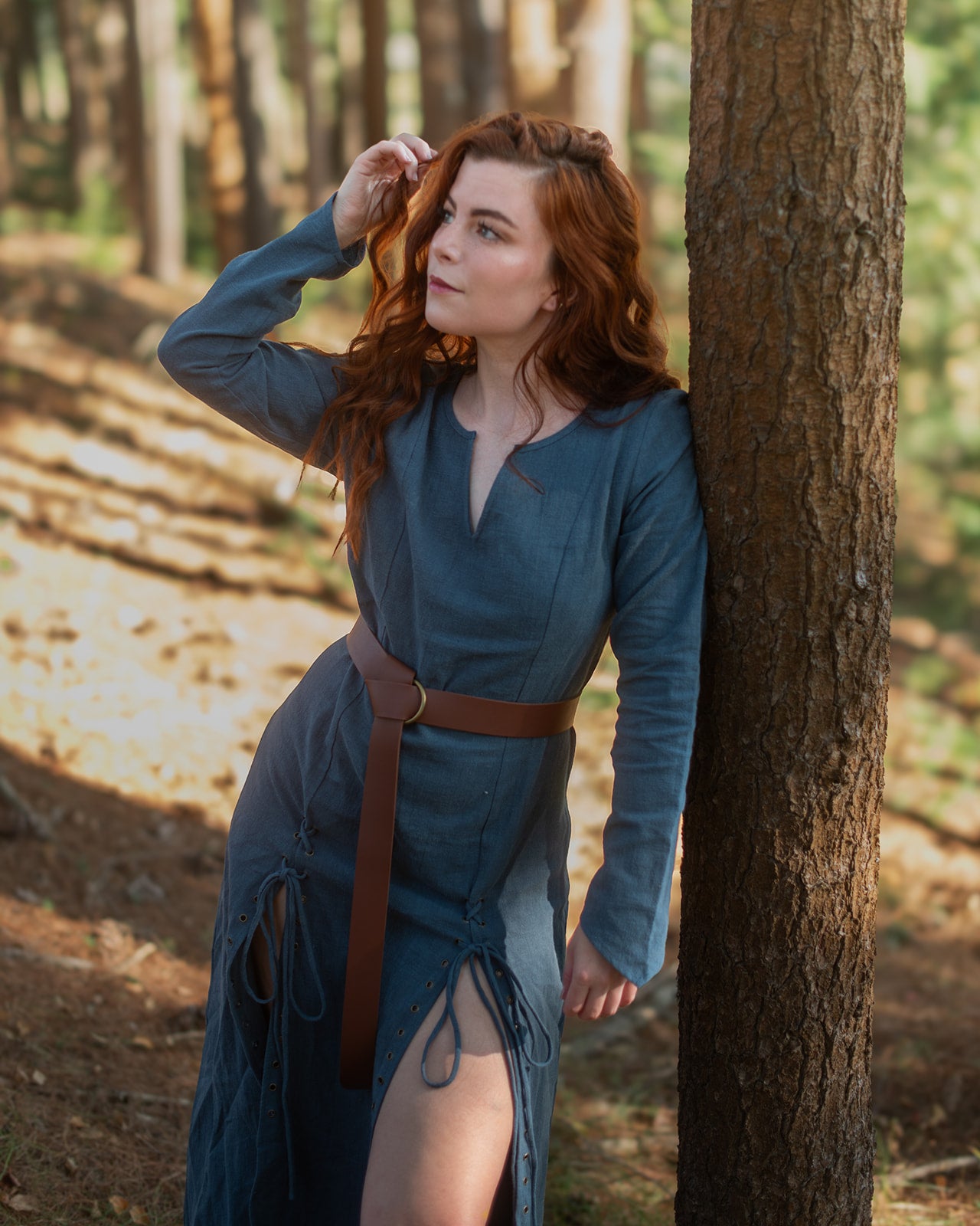 Teal Viking dress with brown leather belt shown outdoors in forest setting with laced front detail and fitted silhouette