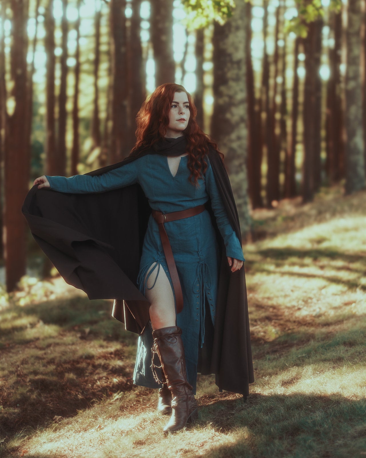 Teal Viking dress with black cloak shown in forest setting, featuring laced front, leather belt and knee-high boots