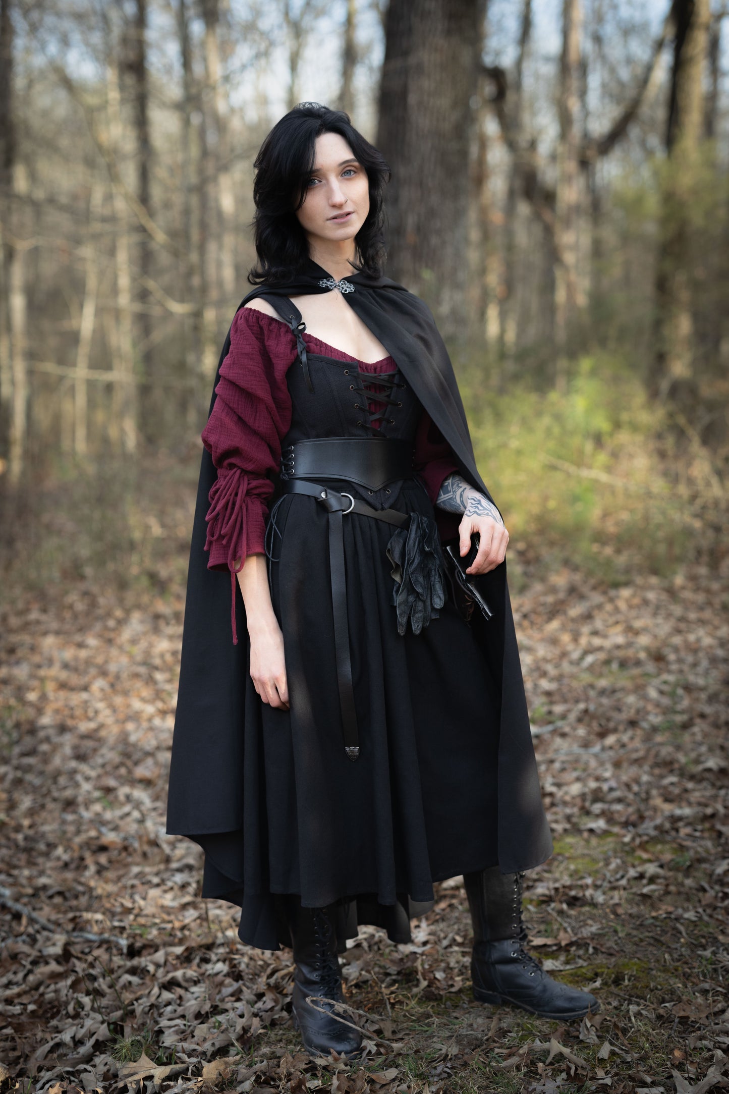 Linen Renaissance Cloak shown in forest setting with black flowing fabric and burgundy sleeve, paired with medieval-style dress and belt