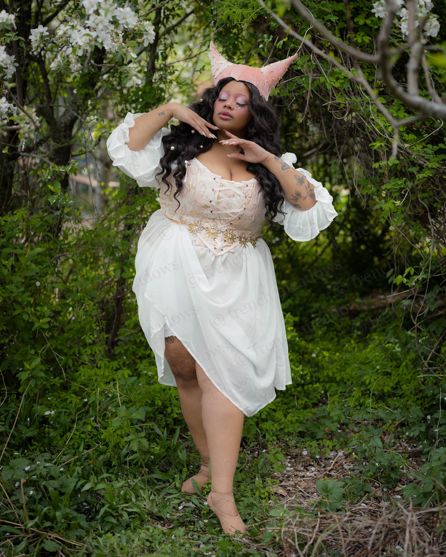 Pink and Gold Metallic Floral Corset Top worn with white flowing dress in a forest setting by a woman posing gracefully.