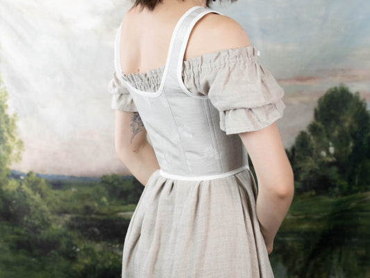 Back view of a woman wearing a Handmade Beige Fern Corset over an off-shoulder linen dress in a natural setting