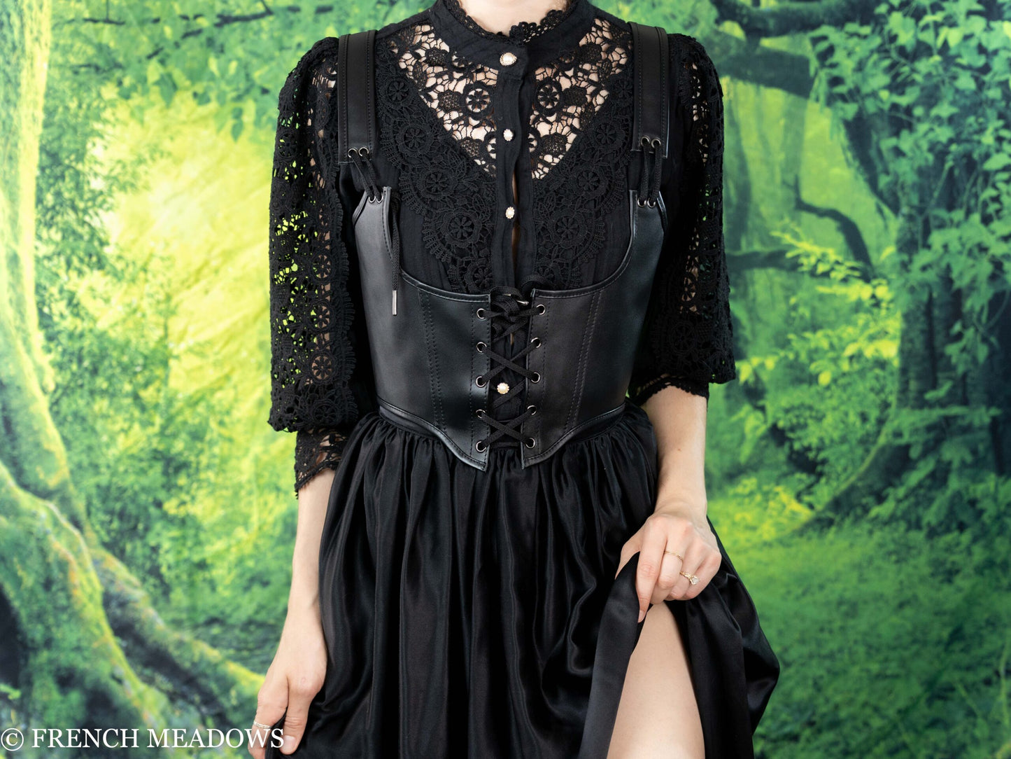 Leather underbust corset belt styled with black lace top and flowing skirt against green forest backdrop