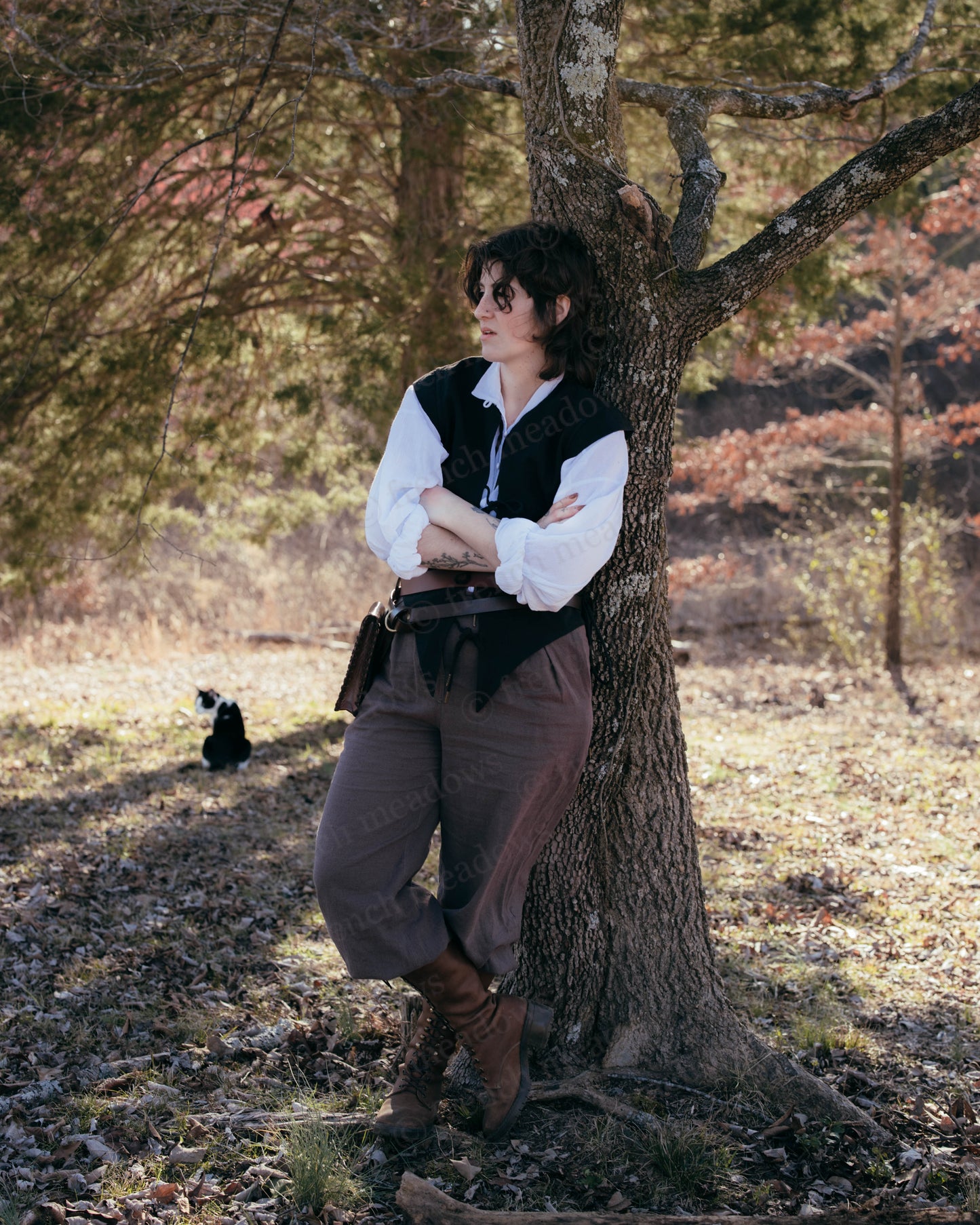 Black Bard Vest shown in outdoor setting with white shirt, brown pants and boots, leaning against autumn tree