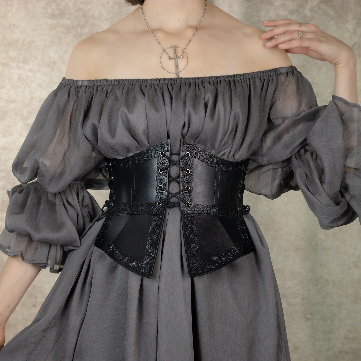 Debossed leather underbust corset with medieval pattern worn over gray off-shoulder dress, showcasing intricate leather detail