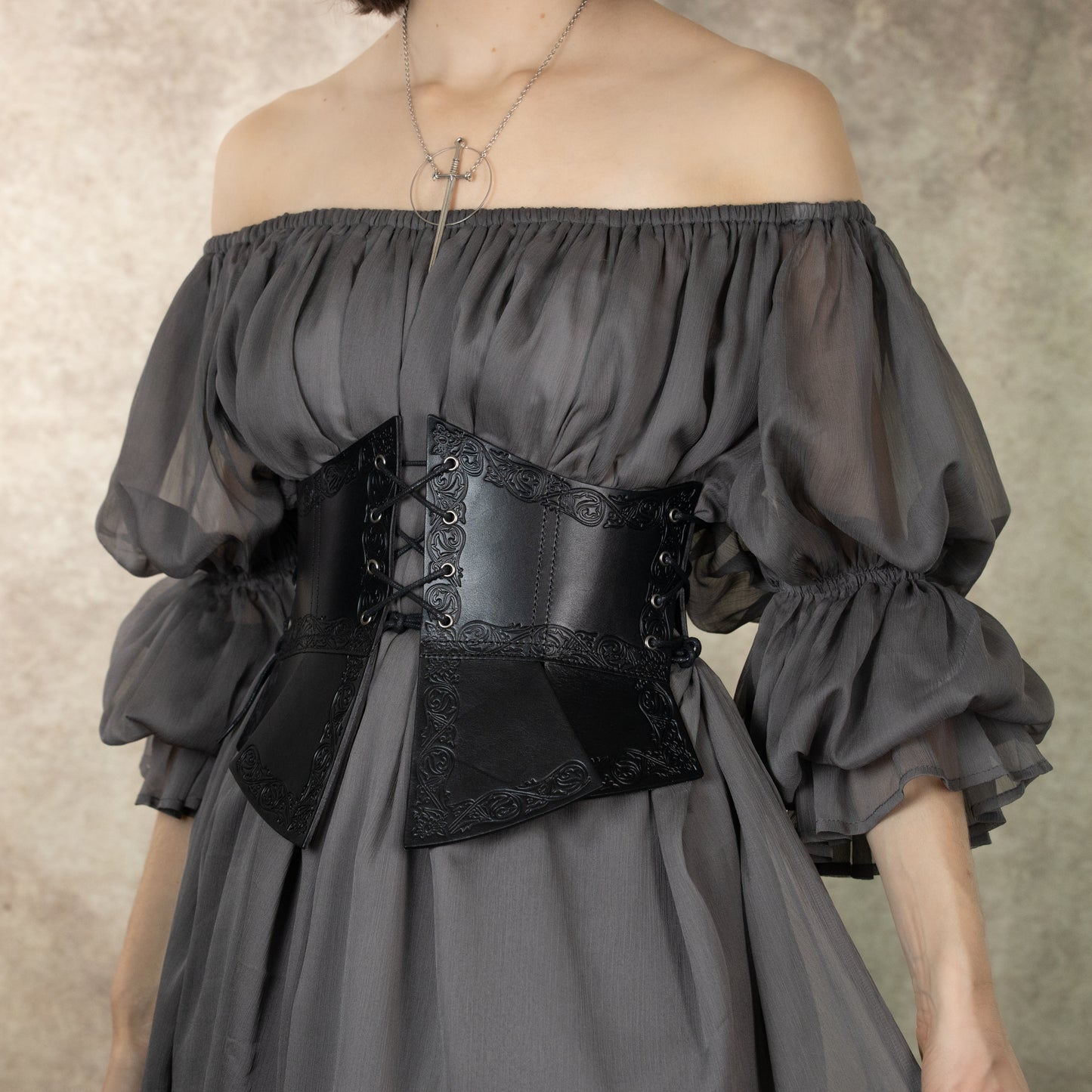 Debossed leather underbust corset with medieval pattern worn over gray off-shoulder dress showing intricate design details