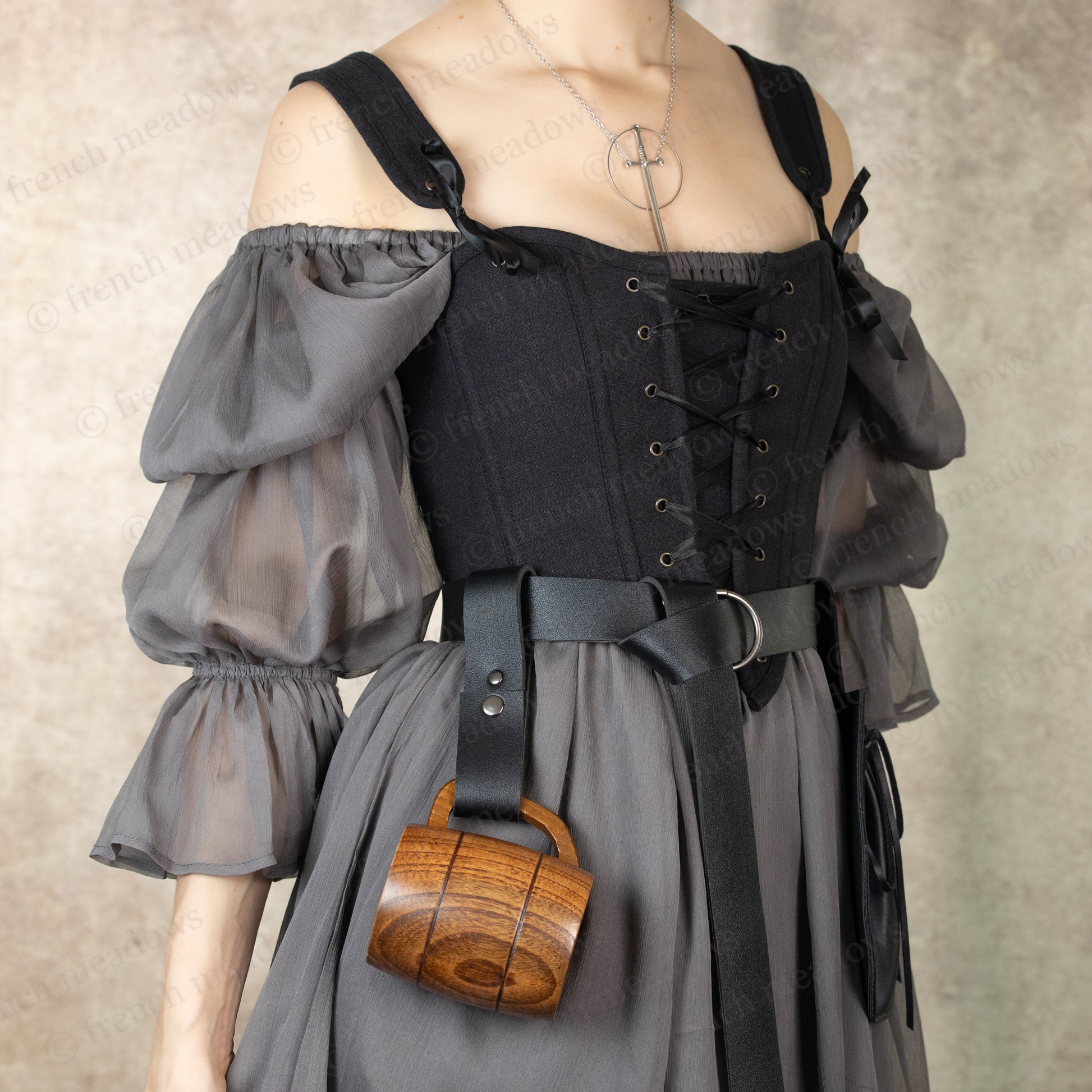 Vegan leather tankard strap attached to medieval dress belt, holding wooden mug against gray renaissance costume