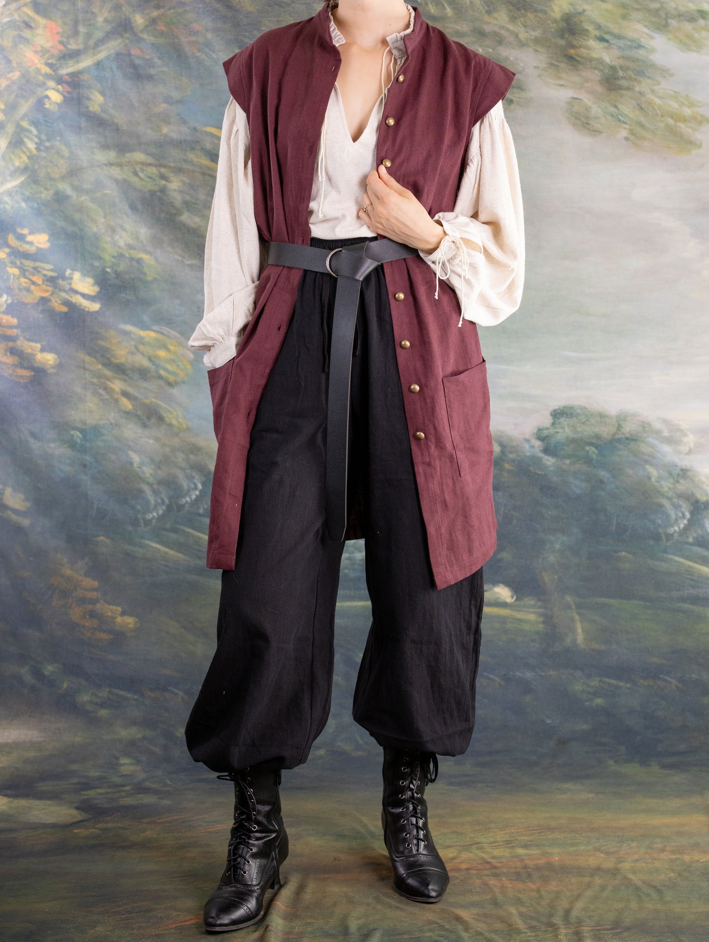 Model wearing rustic black Pirate Pants paired with lace-up boots and a sleeveless burgundy vest over a loose cream shirt