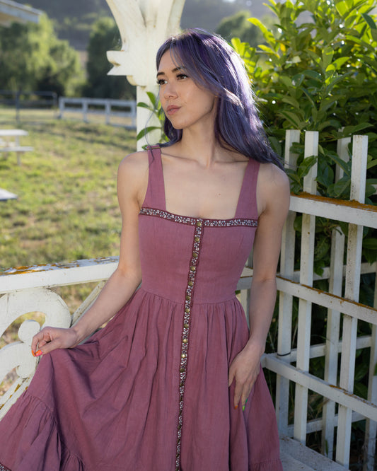 Woman wearing a blackberry-colored dirndl dress with bronze snap buttons and adjustable lace-up back in outdoor garden setting