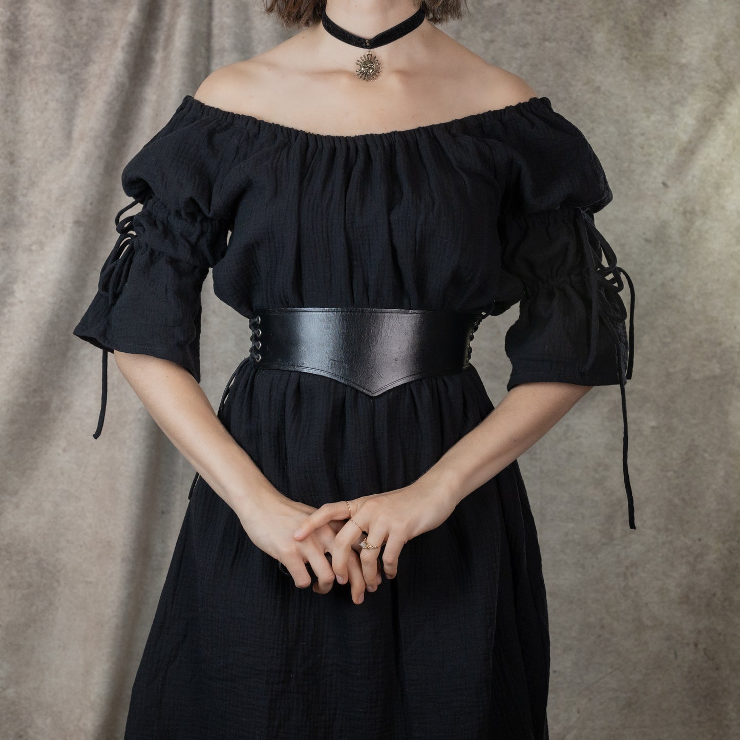 Wide leather waist belt shown on black off-shoulder dress with medieval style lacing details and antique-inspired design
