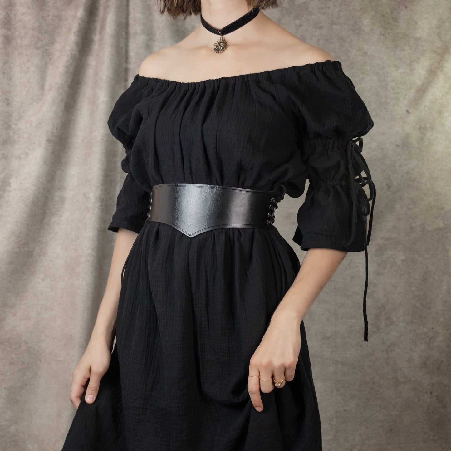 Wide leather waist belt shown on black off-shoulder dress, featuring medieval-style design with side lacing and carved details