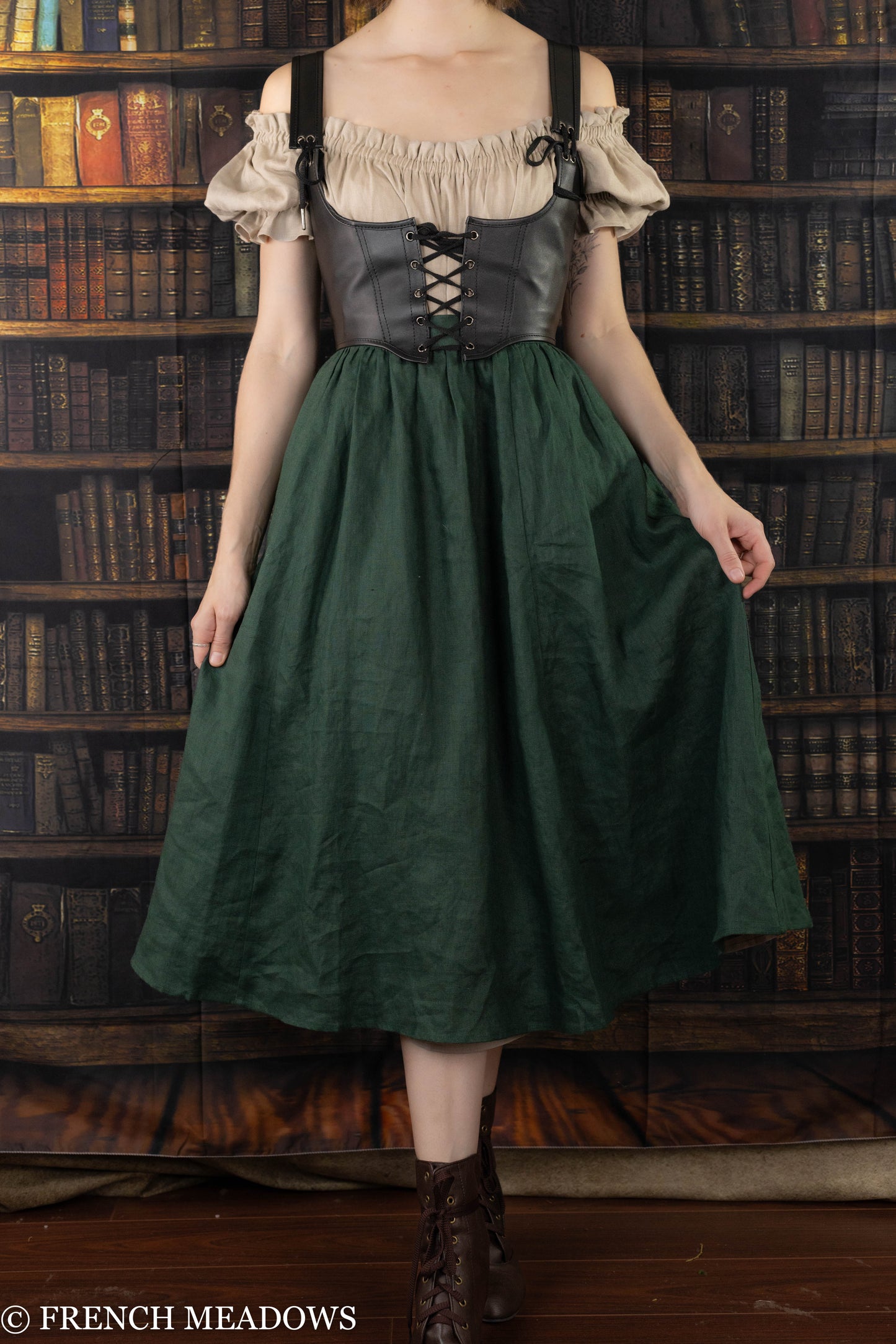 Leather underbust corset belt paired with cream peasant top and forest green skirt against vintage library background