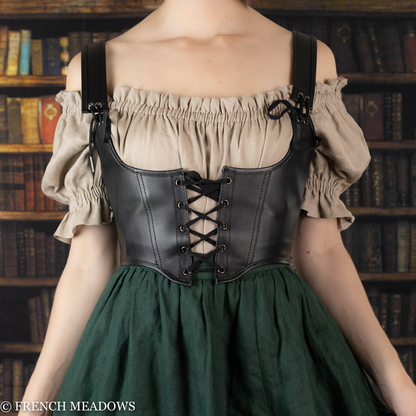 Leather underbust corset belt shown on mannequin with peasant blouse and green dress against vintage bookshelf background