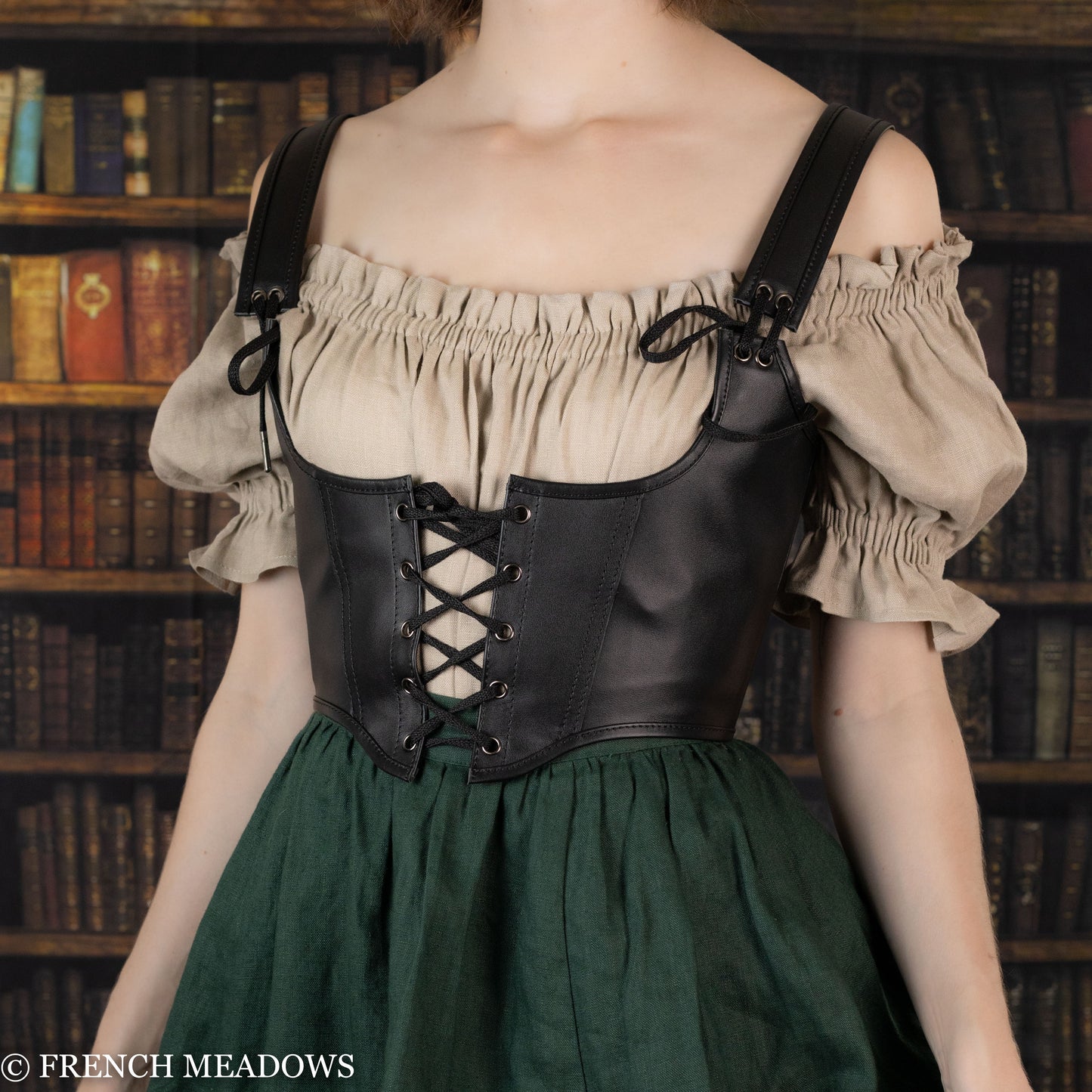 Leather underbust corset belt worn over beige peasant top and green skirt, shown against vintage library background