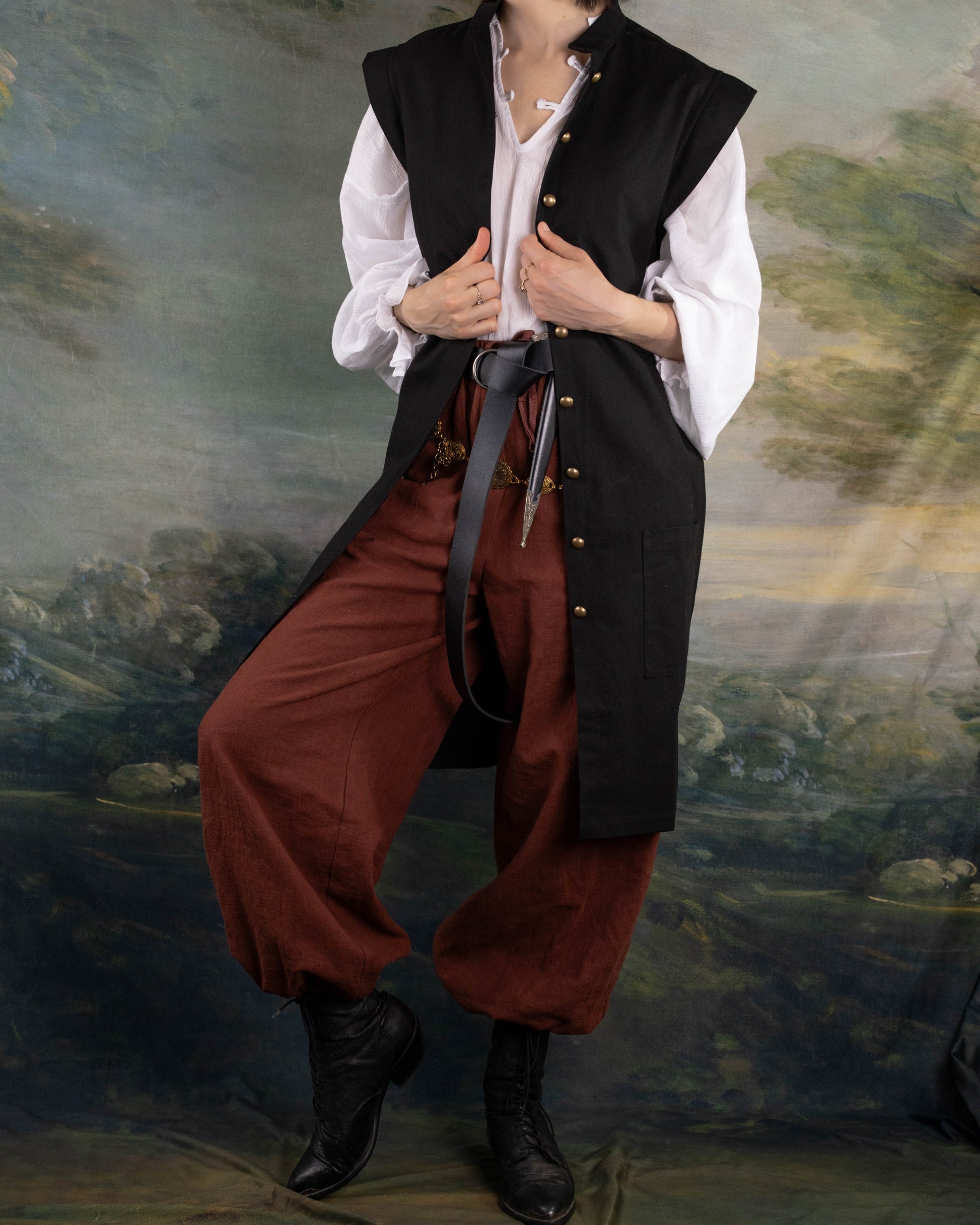 Black Pirate Vest worn over white shirt with brown pants and black boots against painted backdrop.