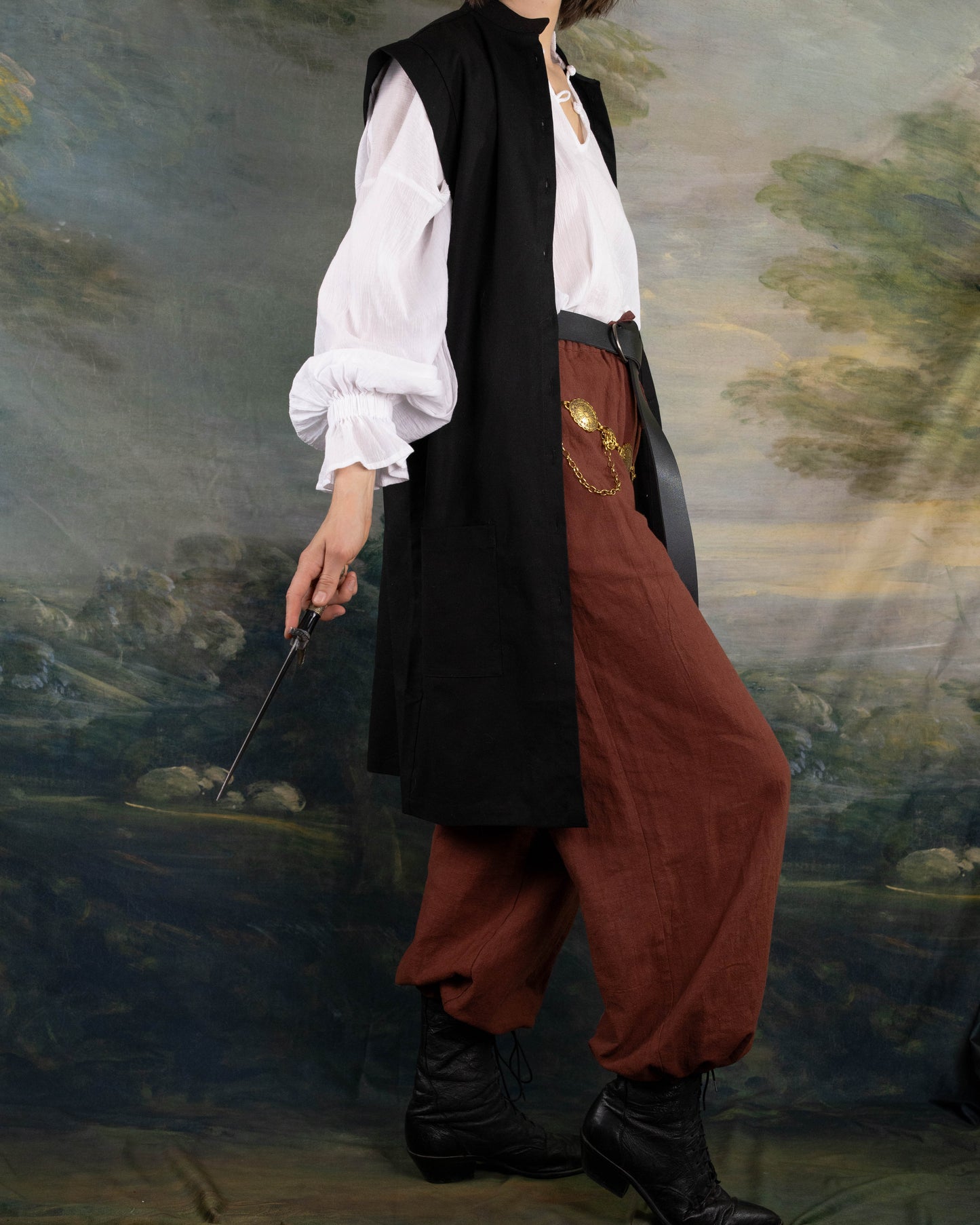 Model wearing a Black Pirate Vest over a white shirt with brown pants and black boots, holding a thin sword.