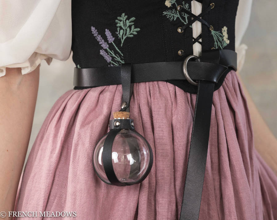 Potion bottle holder with black leather strap attached to embroidered corset and pink skirt, displaying clear spherical vial