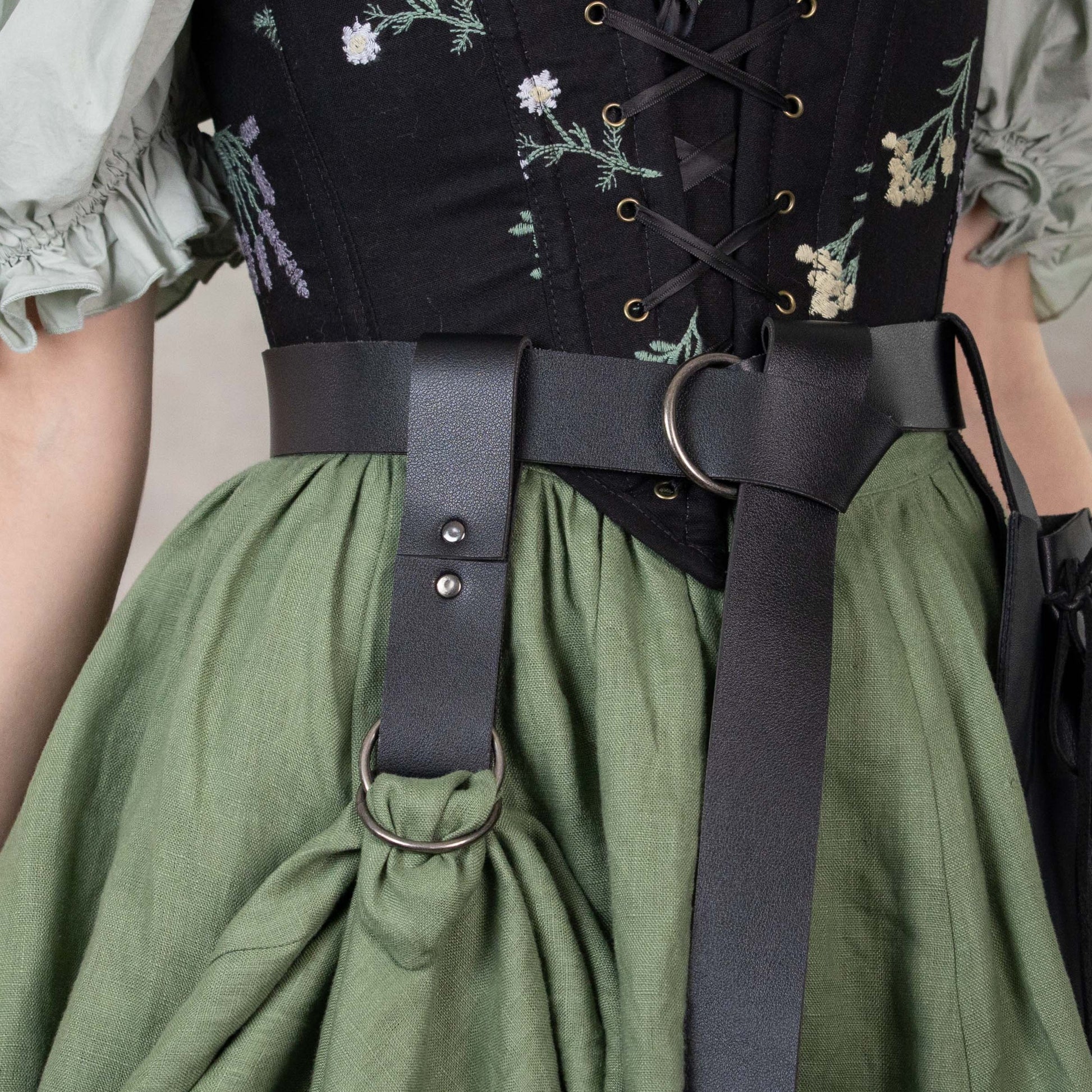 Vegan leather skirt hikes shown on black corset and green renaissance dress, attached to belt with metal D-rings