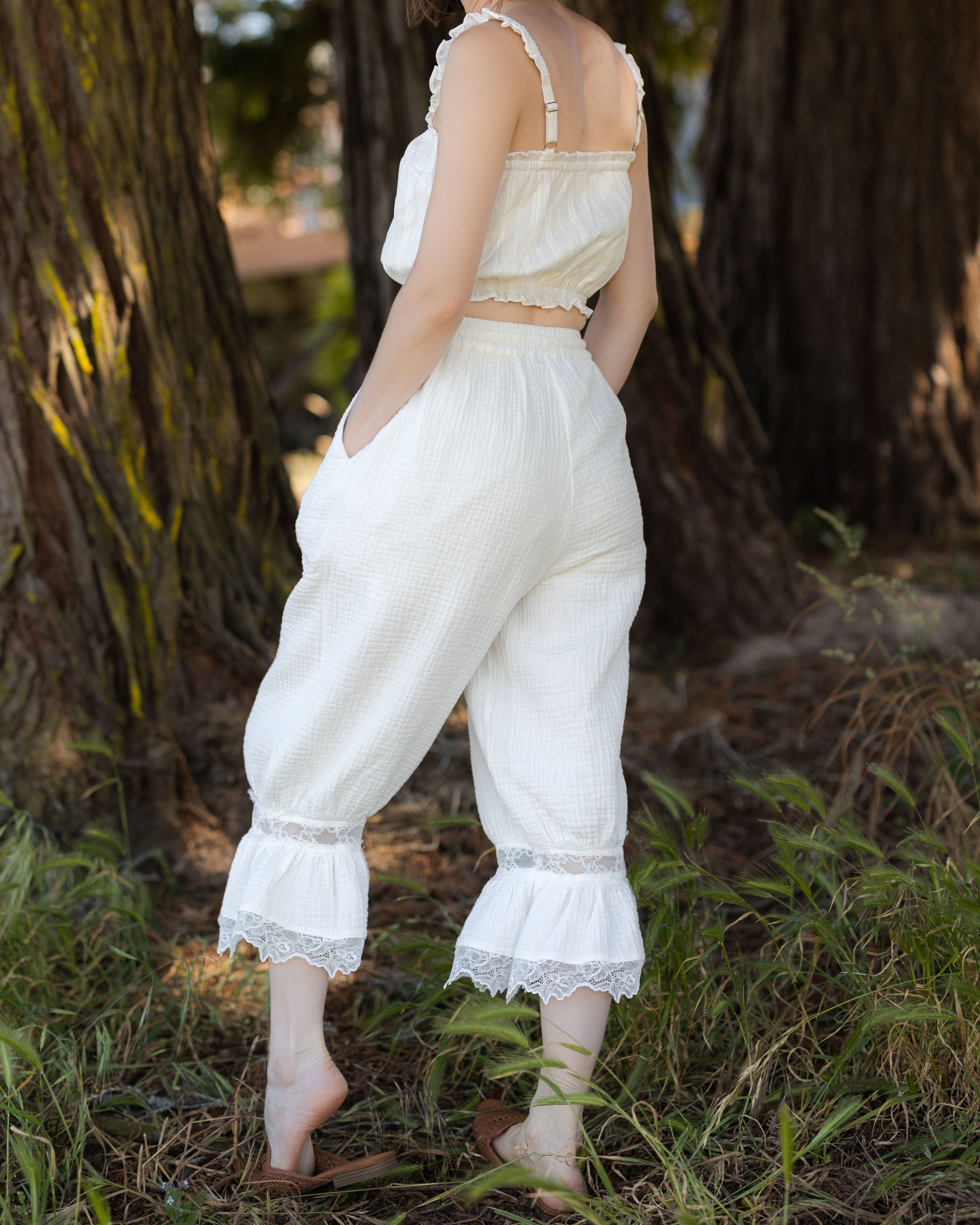 Woman wearing white cotton bloomer pantaloons with lace ruffle hem standing outdoors by trees