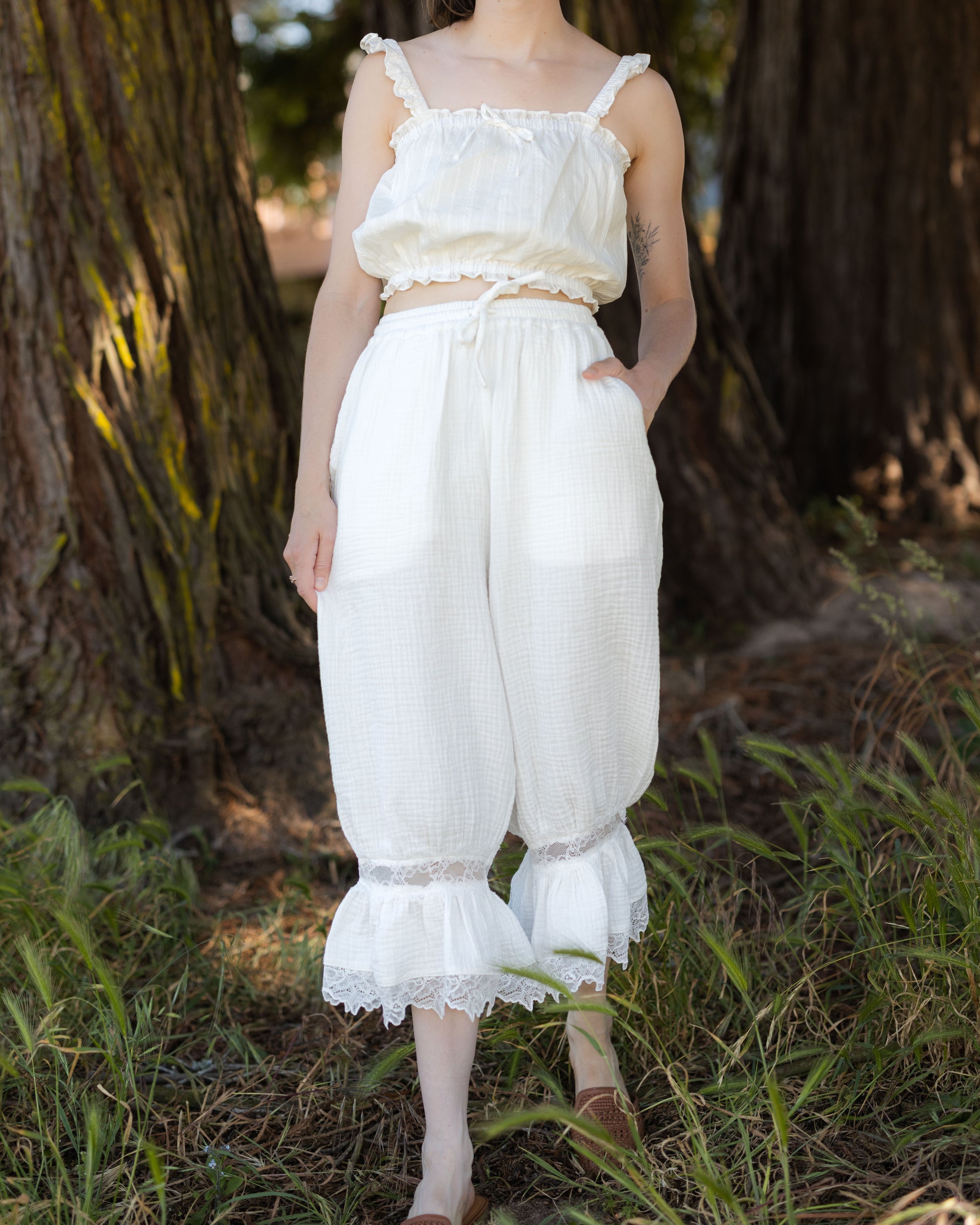 Woman outdoors wearing white cotton bloomer pantaloons with lace ruffle hems and pockets, styled with matching top