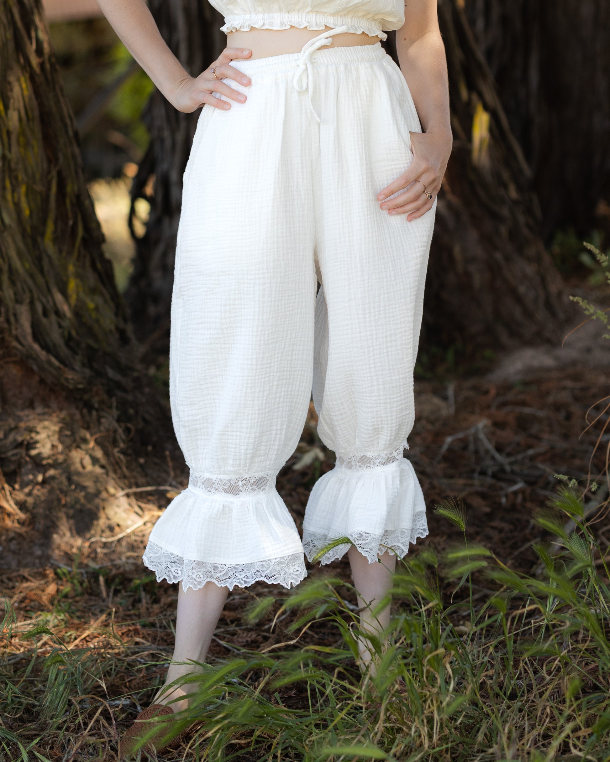 White cotton bloomer pantaloons with lace ruffle hems, adjustable drawstring waist, and pockets, perfect for layering or pajamas.