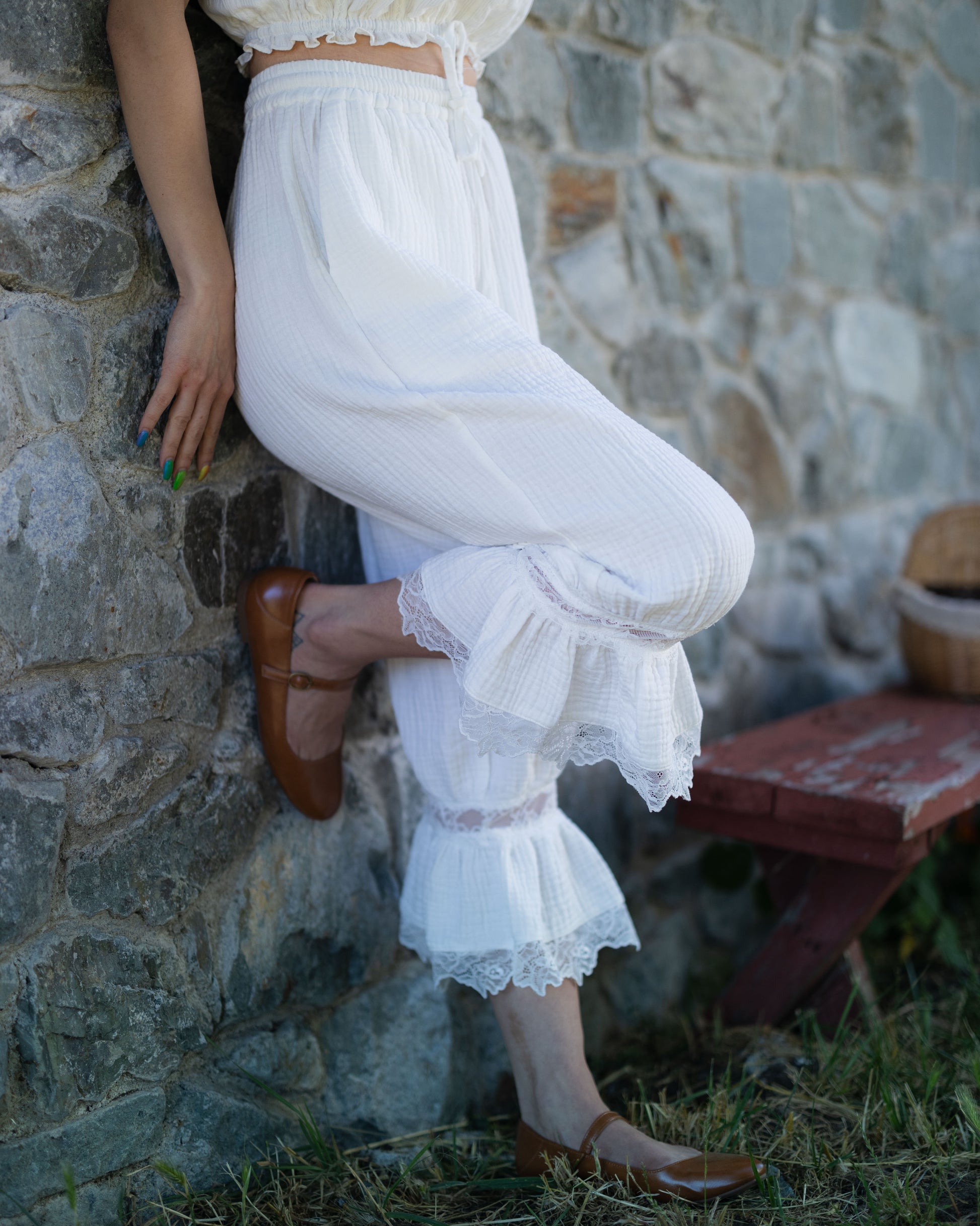 Woman wearing white cotton bloomer pantaloons with lace ruffle hem standing against stone wall outdoors
