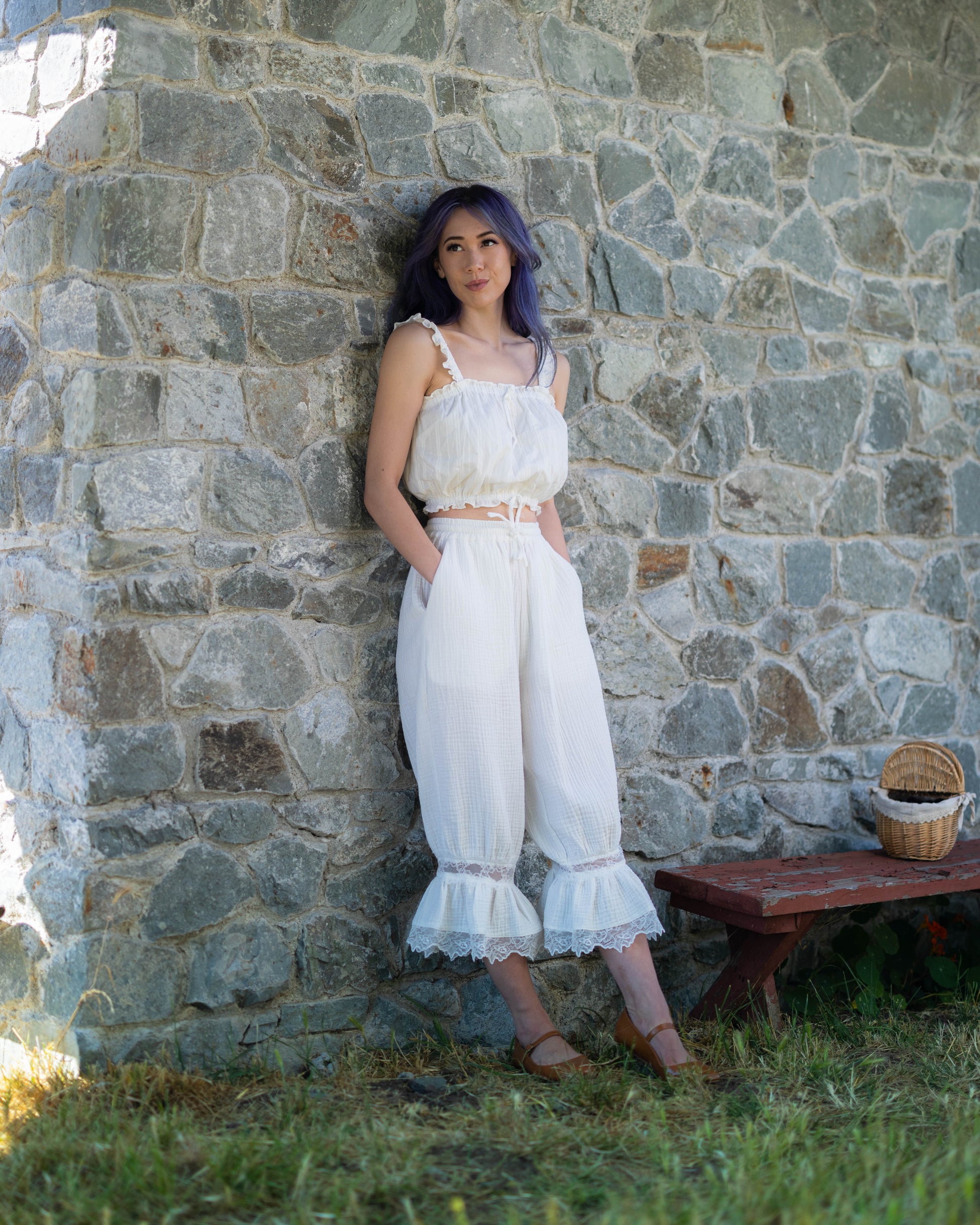 Woman wearing white cotton bloomer pantaloons with lace ruffle hem standing against stone wall outdoors