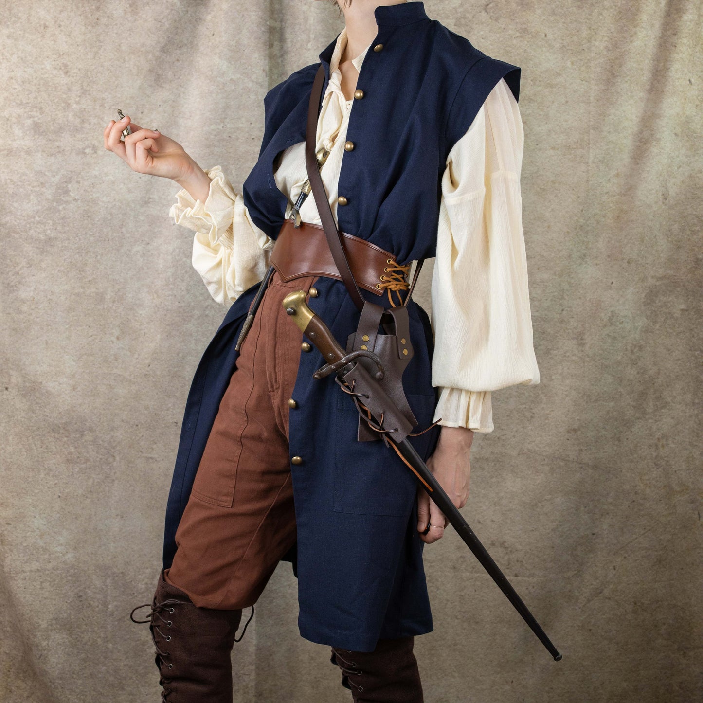 Navy Pirate Vest styled with cream shirt, brown pants and leather belt, shown with decorative sword in historical costume setting