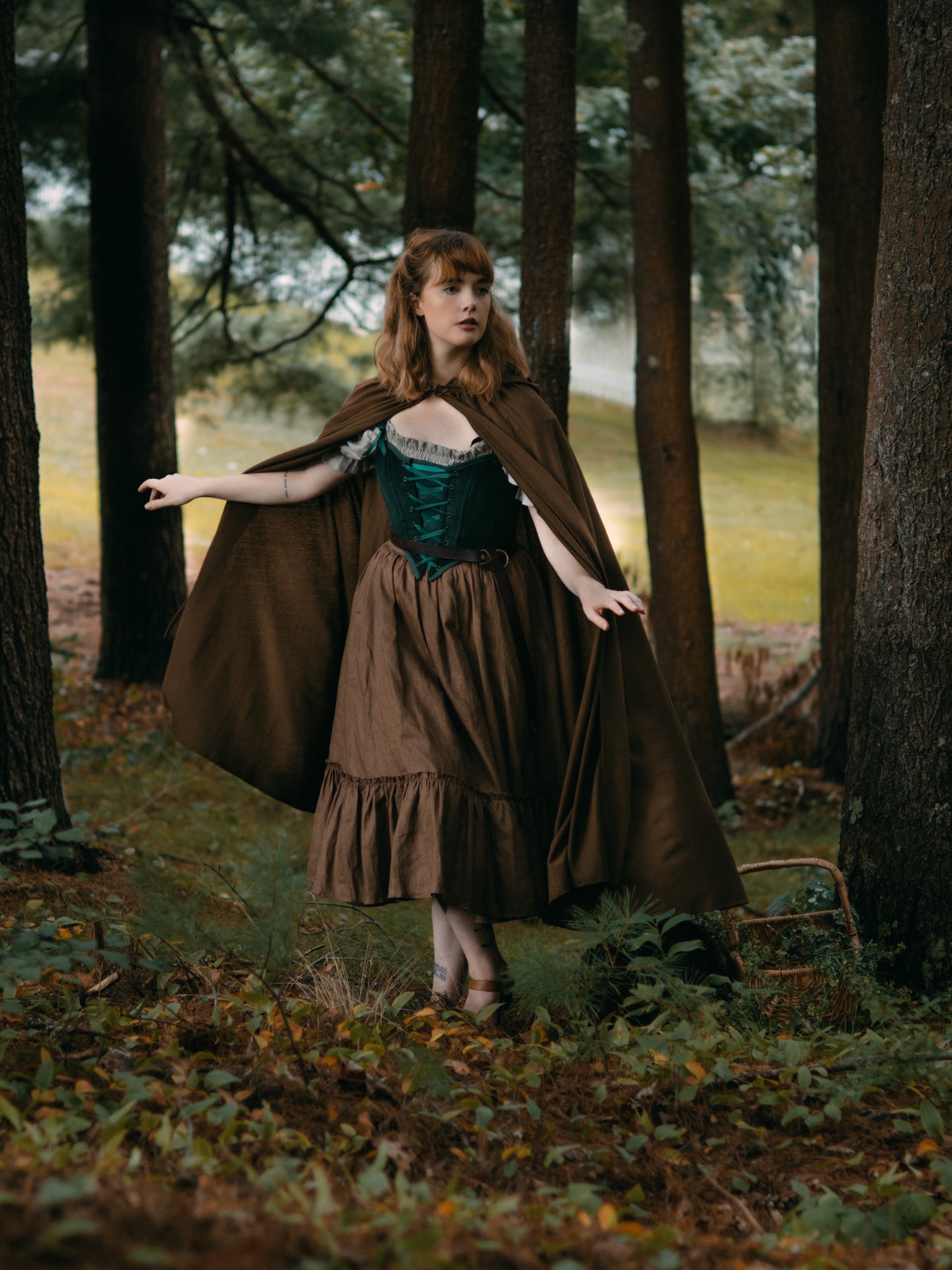 Linen Renaissance Cloak shown flowing in forest setting with medieval-style dress, displaying drape and movement among autumn trees