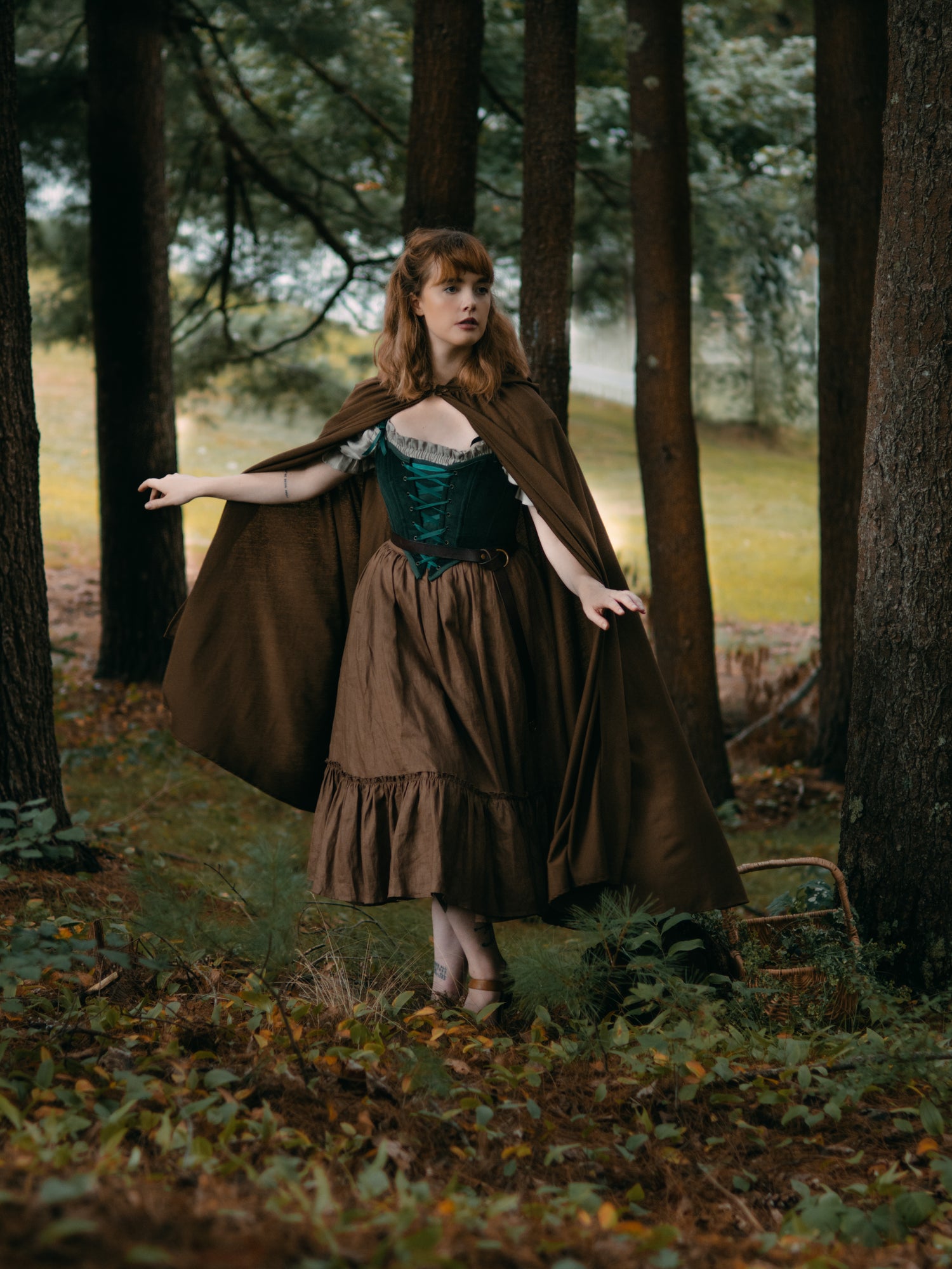 Linen Renaissance Cloak shown flowing in forest setting with medieval-style dress, displaying drape and movement among autumn trees