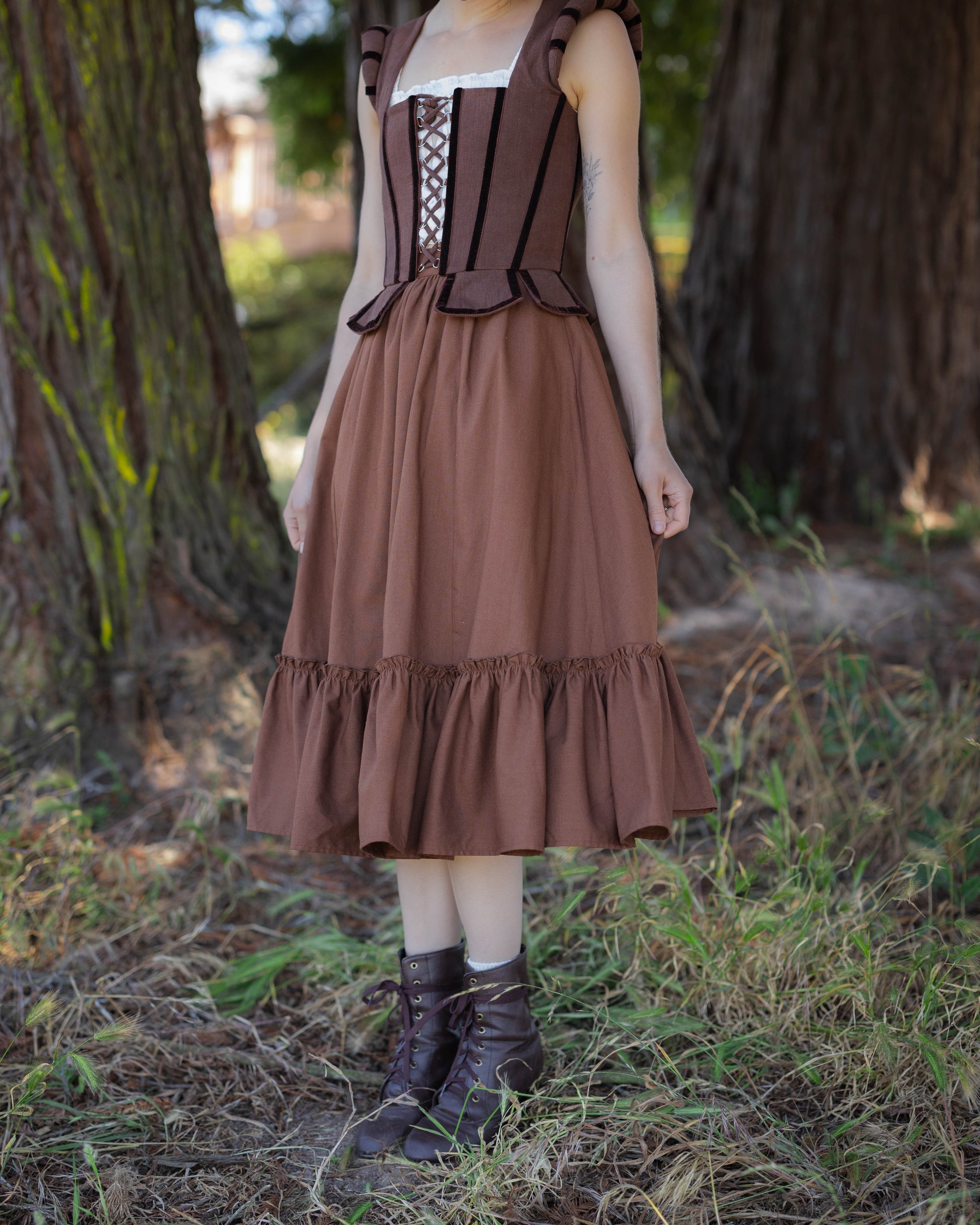 Woman wearing a brown linen ruffle skirt and corset standing outdoors among trees and grass.