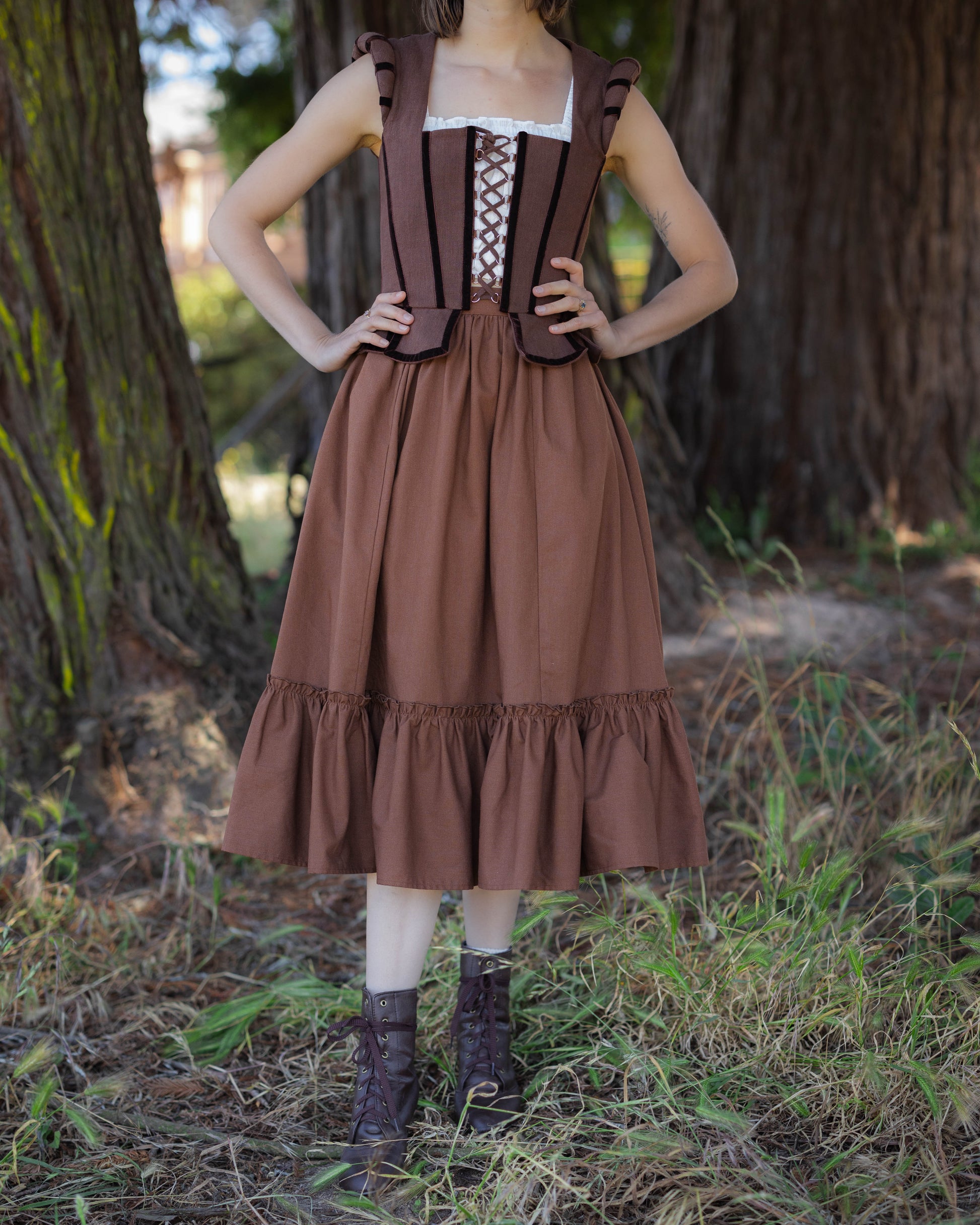 Woman wearing a brown linen ruffle skirt styled with a brown corset top and lace-up boots in a forest setting