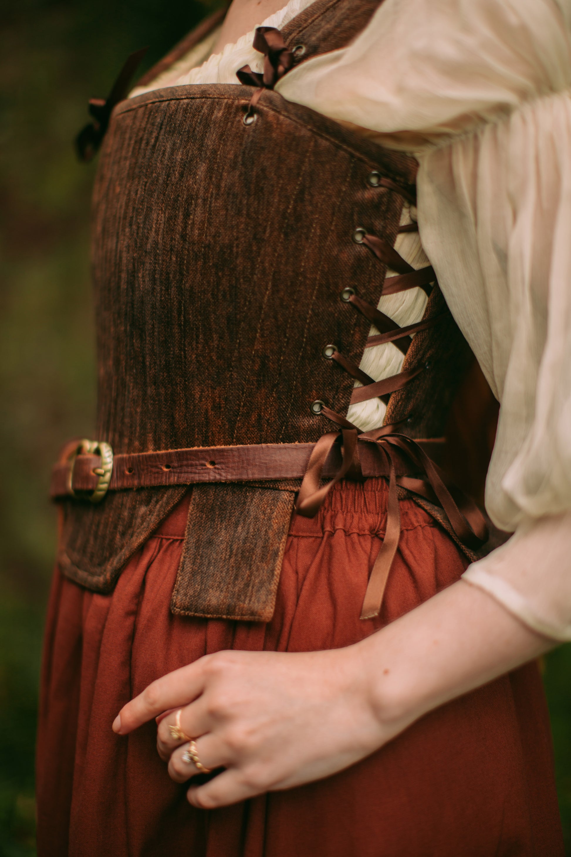 Close-up of brown textured Tudor stays with adjustable side lacing and decorative square waist tabs worn over a blouse.