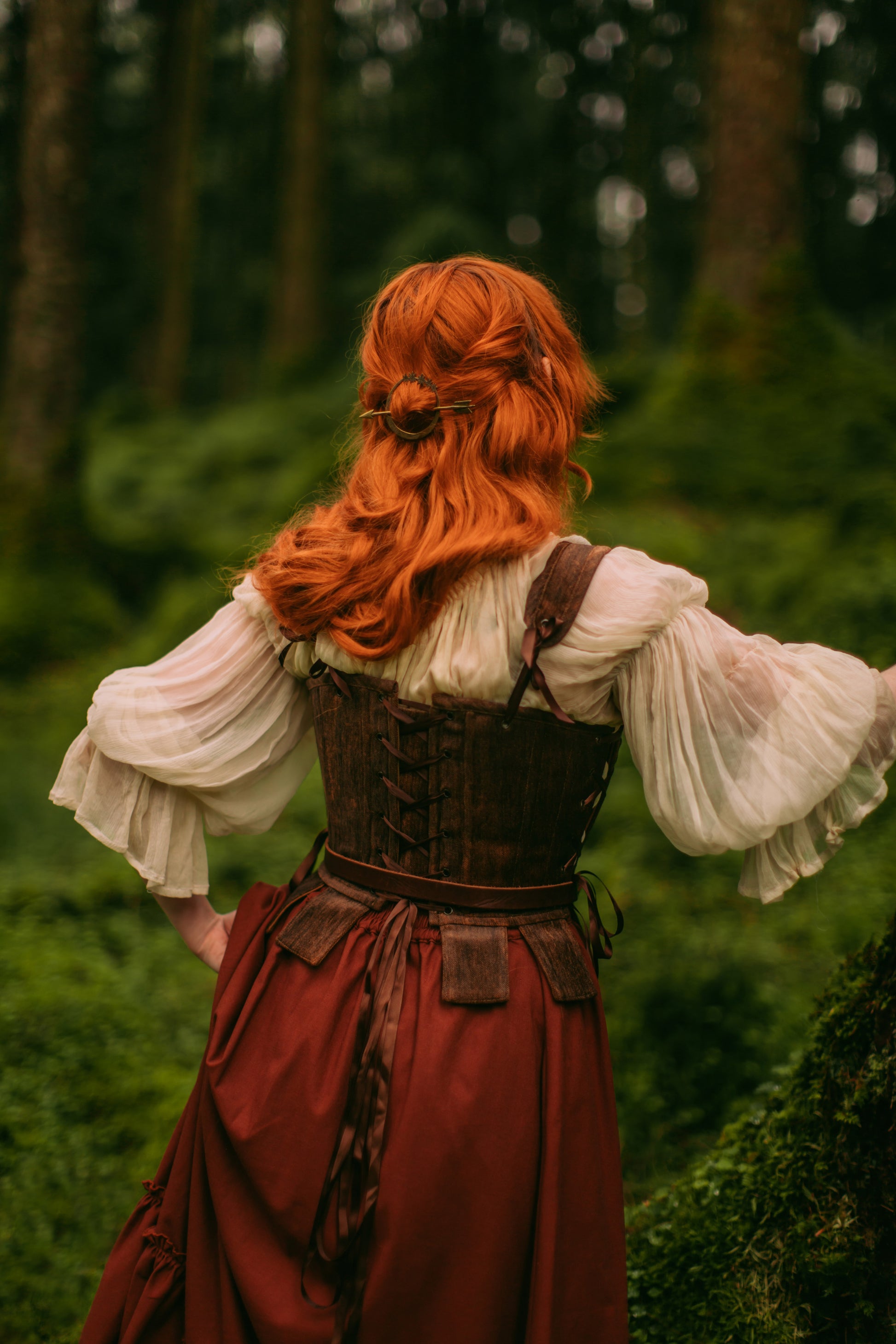 Back view of woman wearing brown tabbed Tudor stays with lace-up details in a forest setting