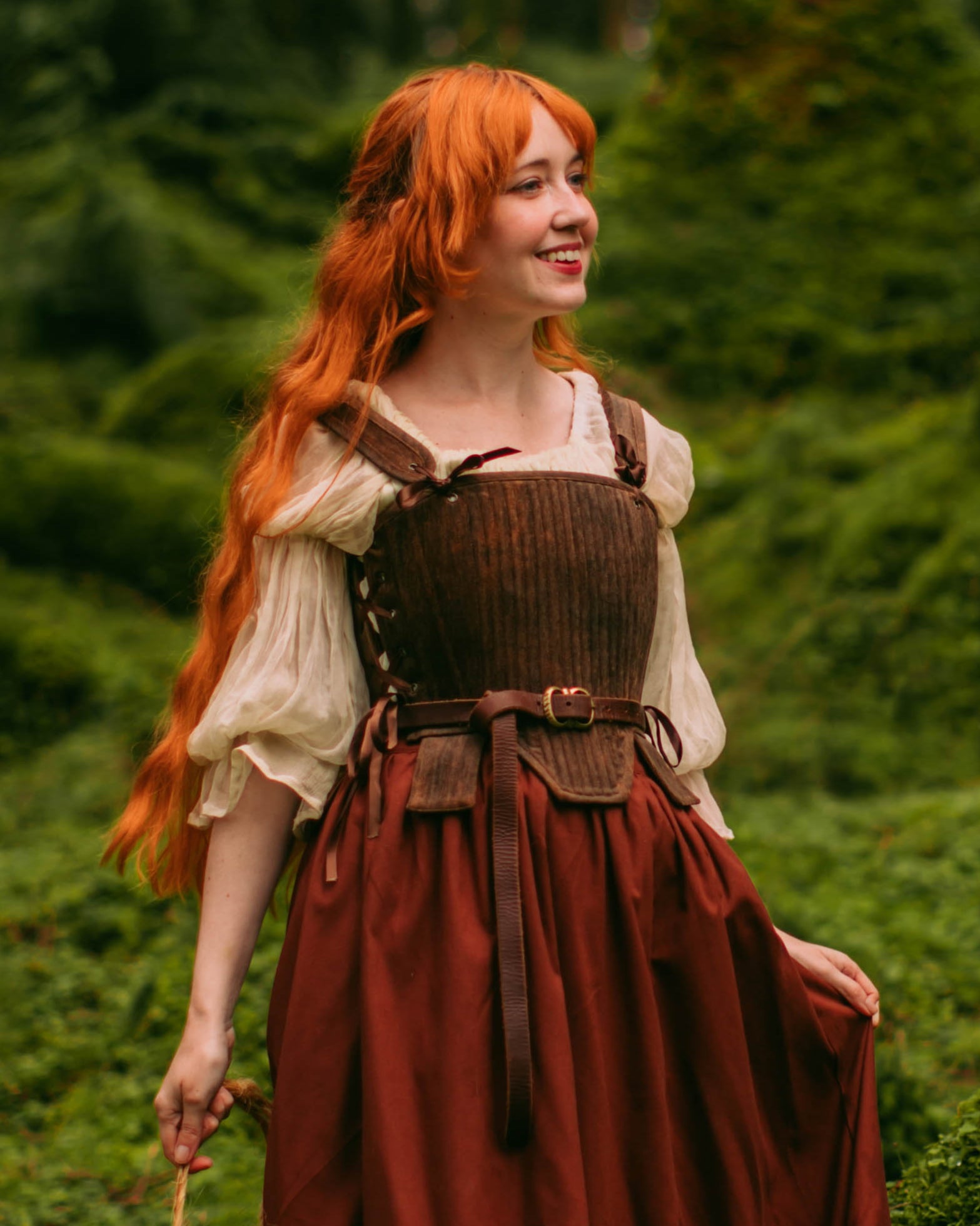 Woman outdoors wearing brown tabbed Tudor stays with long red hair and flowing medieval-style dress