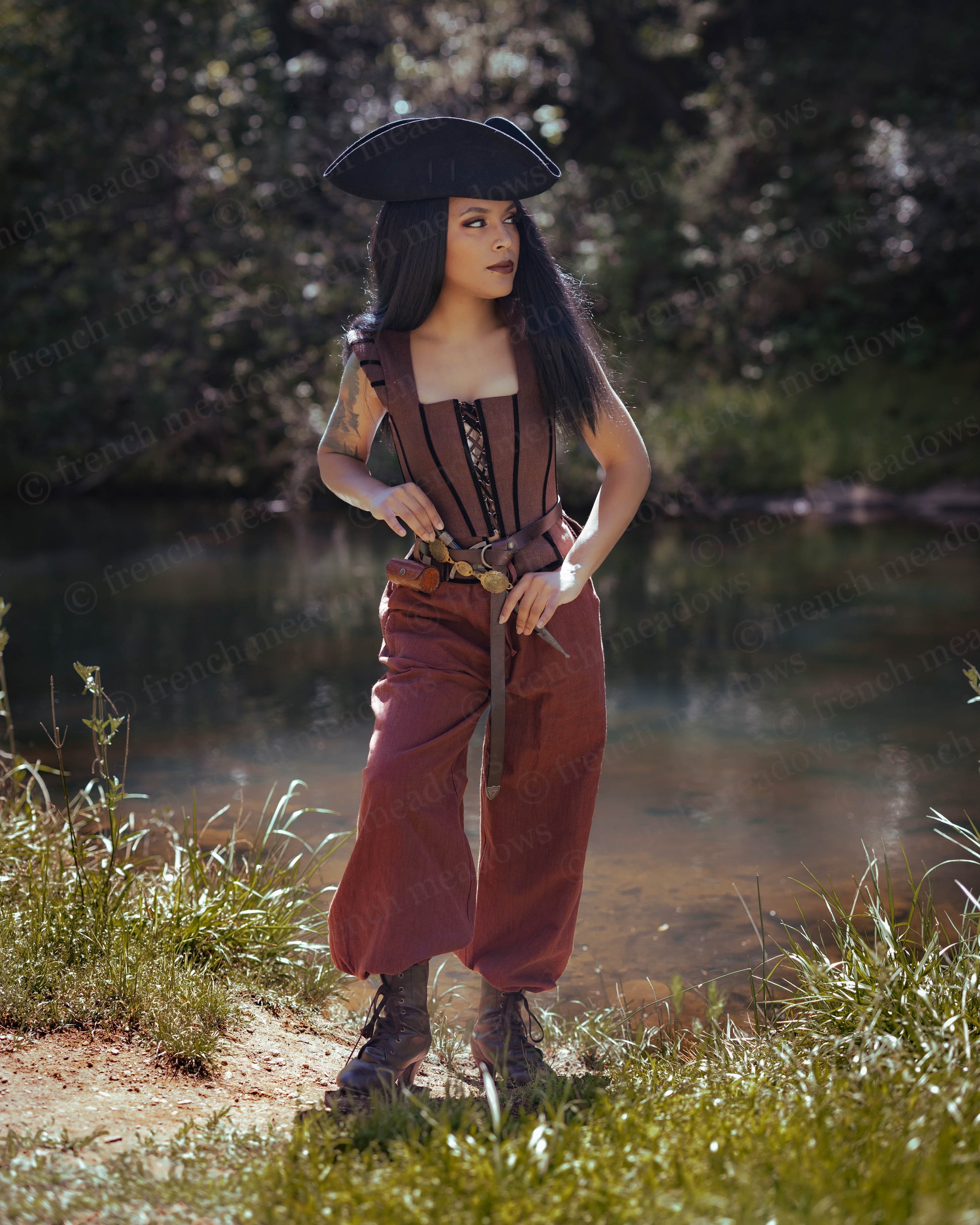 Woman outdoors wearing a rustic brown Tavern Bodice with lace-up front, paired with loose pants and a pirate hat.