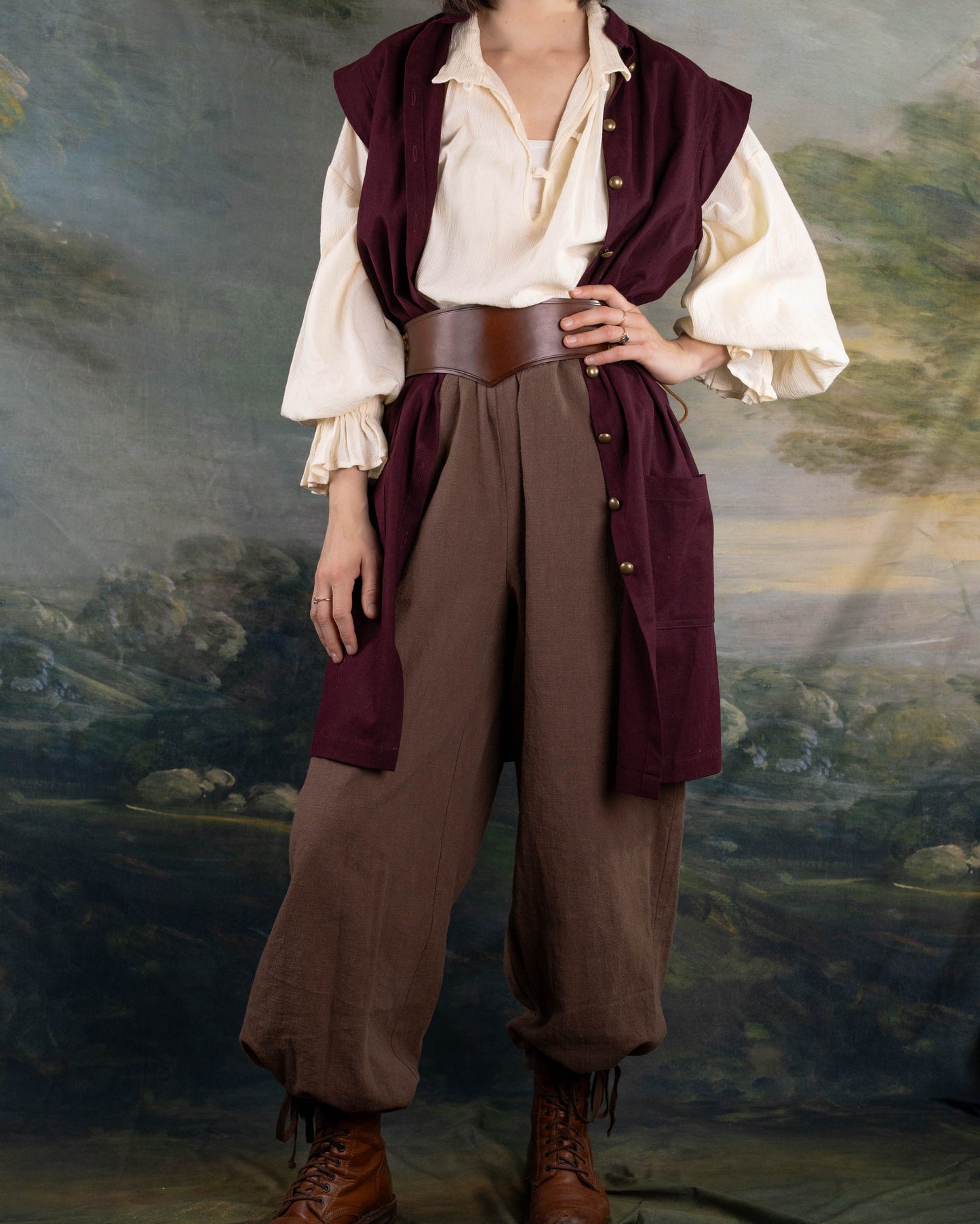 Woman wearing Burgundy Pirate Vest over a cream shirt with brown pants and leather belt in a historical style setting.