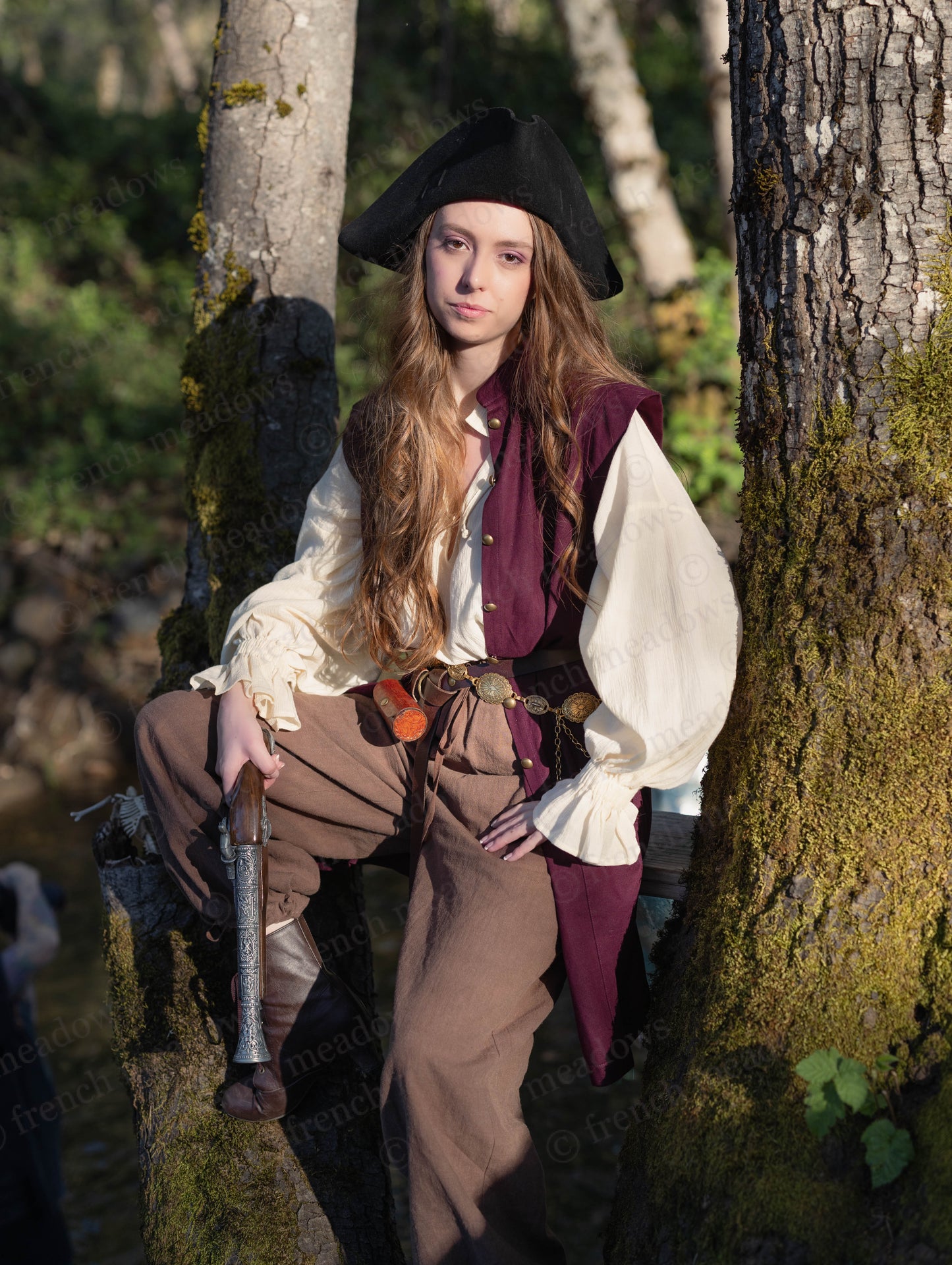 Young woman wearing a Burgundy Pirate Vest with a black hat and medieval costume in a forest setting